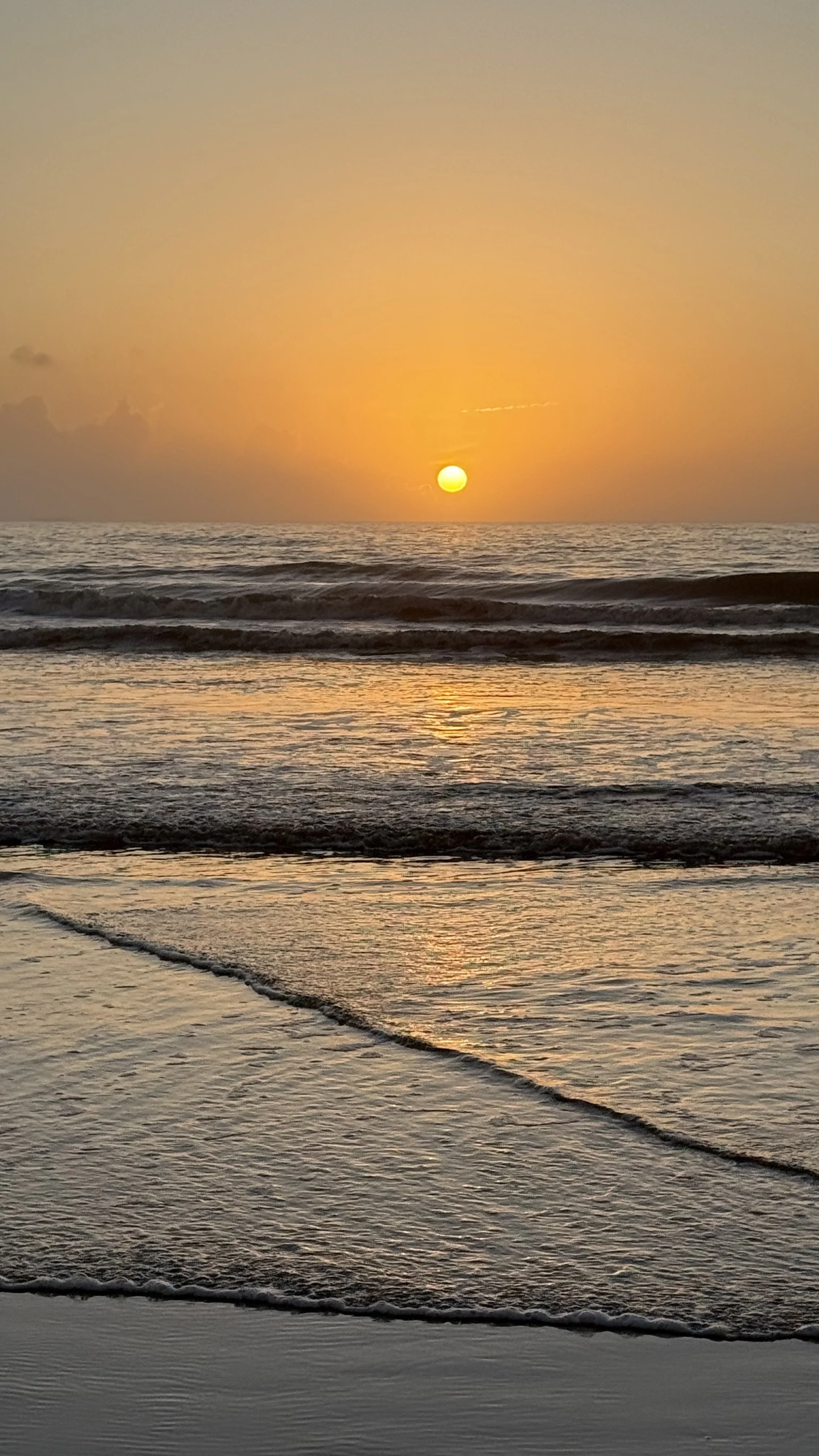 Sunset over the ocean with waves gently rolling onto the beach.