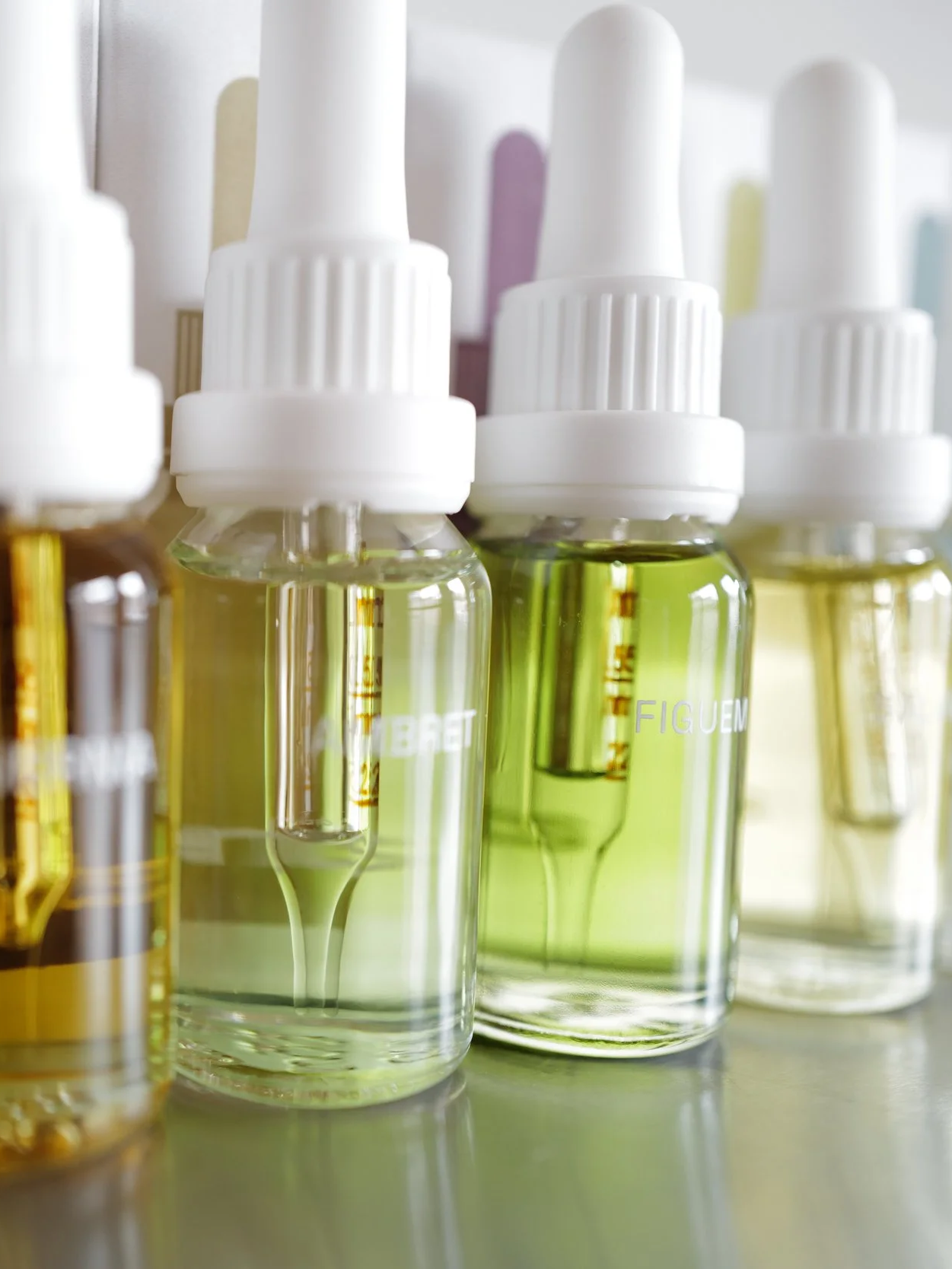 Close-up of glass 15mL diffuser oil bottles with white droppers containing various scent liquids on a reflective surface.