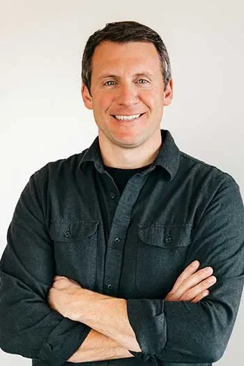 Mark Edgell of Edgell Building. A man smiling with arms crossed, wearing a black button-up shirt, standing against a plain background.