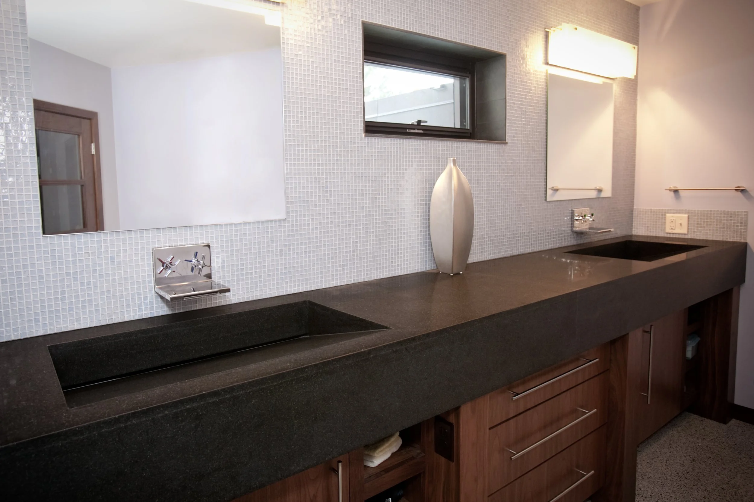 Modern bathroom vanity with double black sinks, large mirror, small window, and wooden cabinetry. Custom Home built in Montana by Edgell Building.
