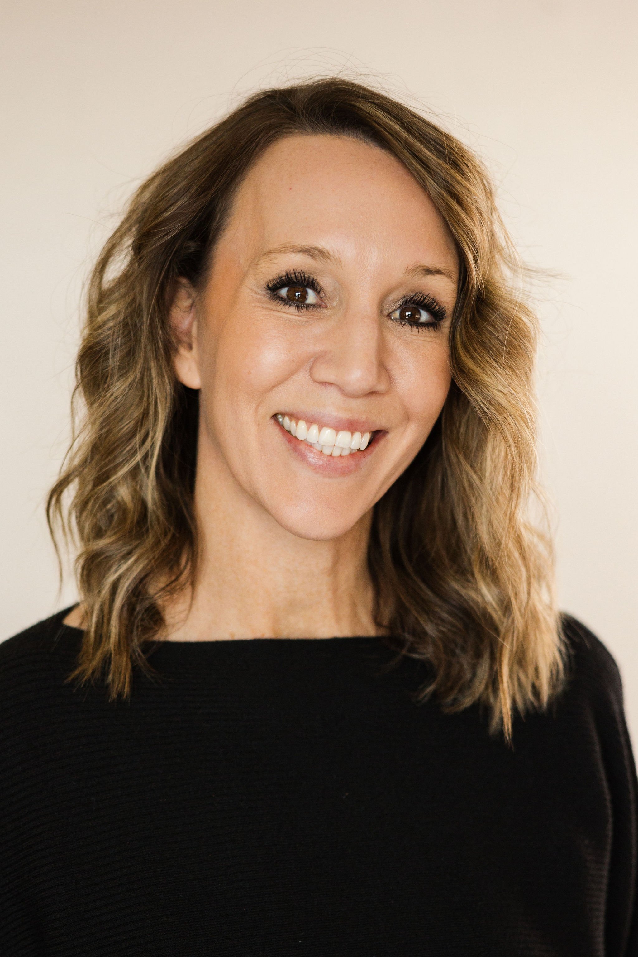 Austen Davis of Edgell Building. A woman with shoulder-length wavy light brown hair smiling at the camera, wearing a black top against a plain light-colored background.