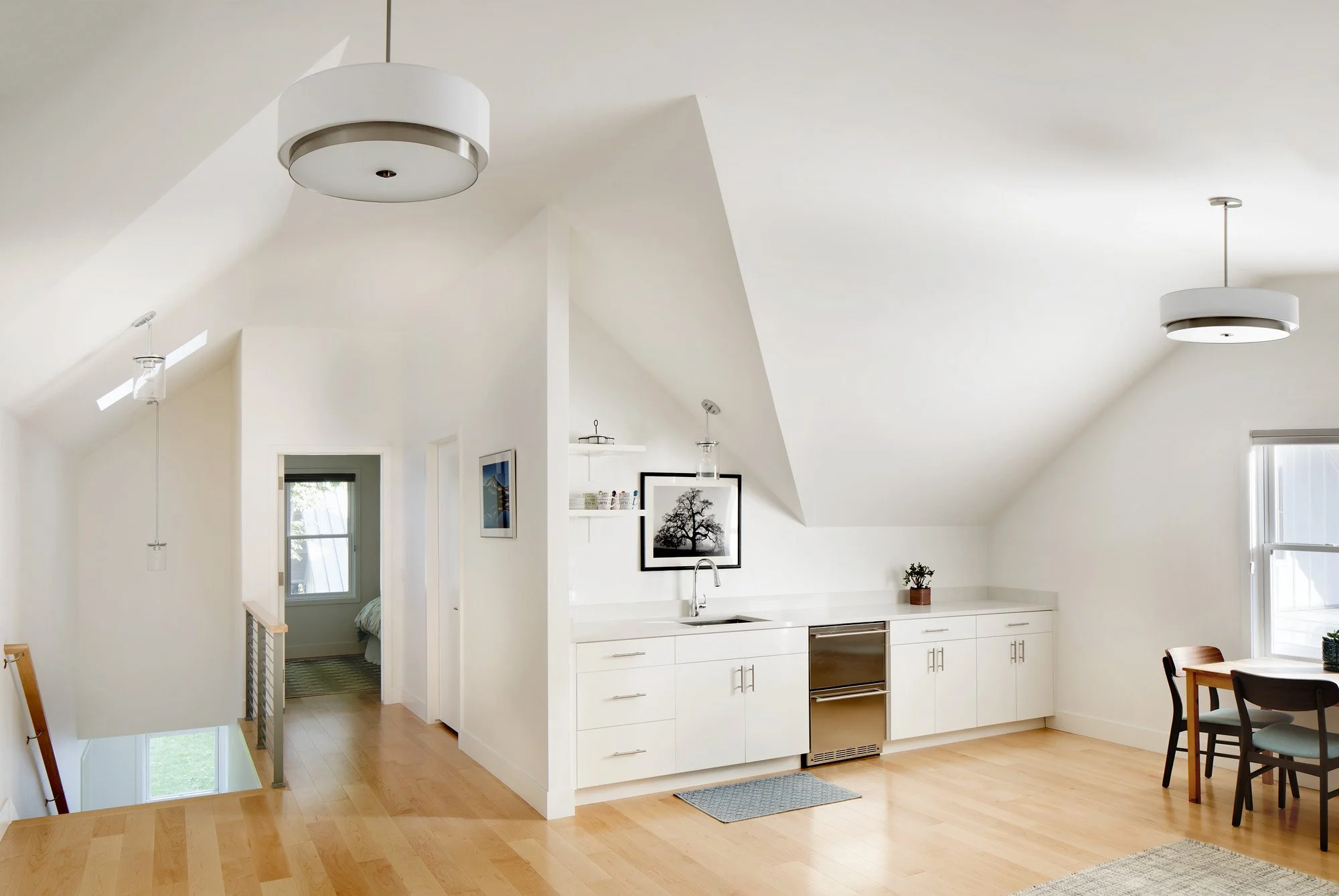Kitchen area with white cabinets, wooden flooring, a small refrigerator, and a dining table with chairs in a bright room with sloped ceilings and pendant lighting. Custom Home built in Montana by Edgell Building.