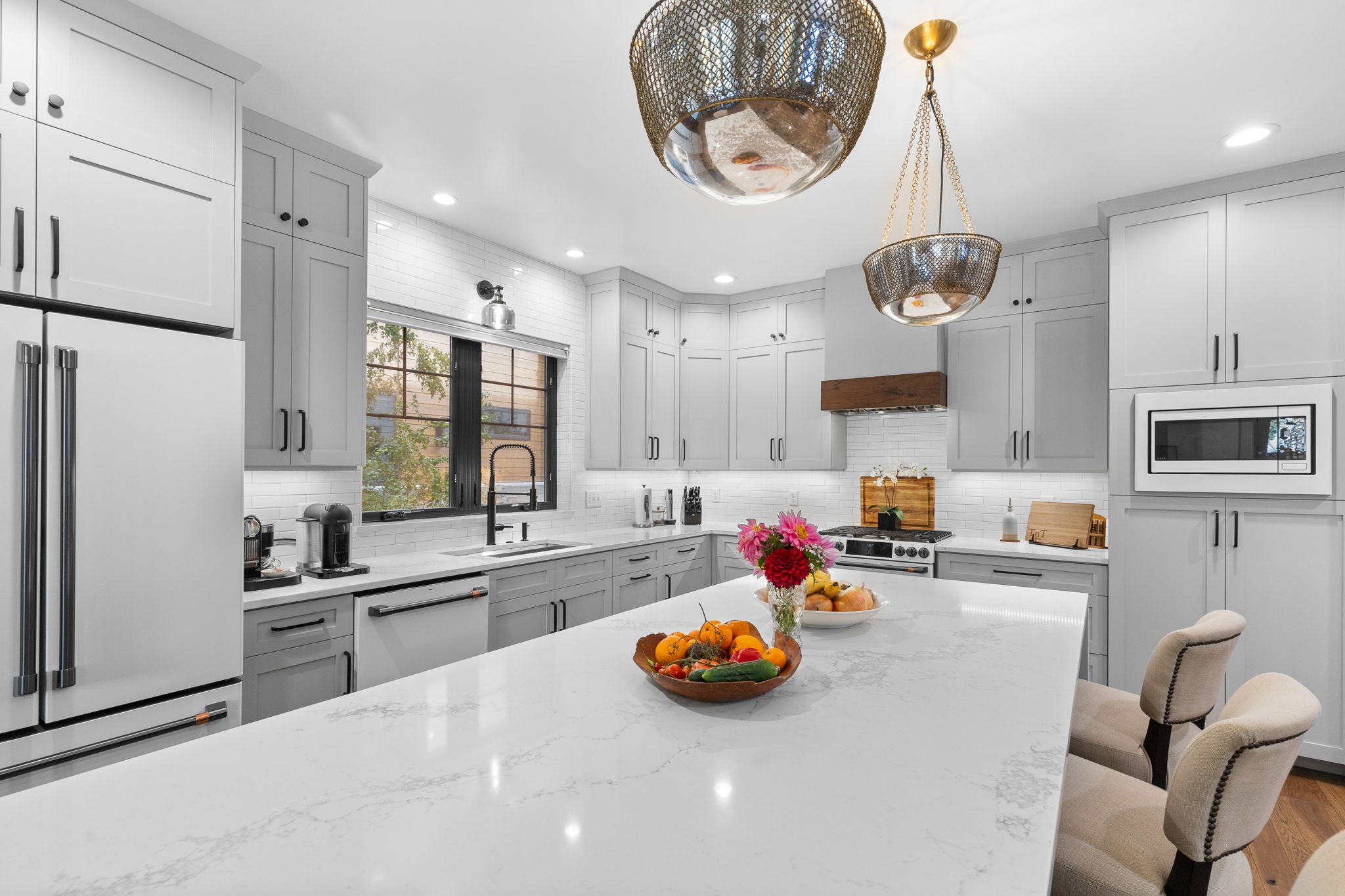 Modern kitchen with white cabinets, a large island with a marble countertop, stainless steel appliances, a window above the sink, and decorative pendant lights. Custom Home built in Montana by Edgell Building.