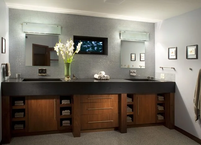 Bathroom vanity with a black countertop, a vase of white flowers, folded towels, two mirrors, framed artworks, and a window Custom Home built in Montana by Edgell Building.