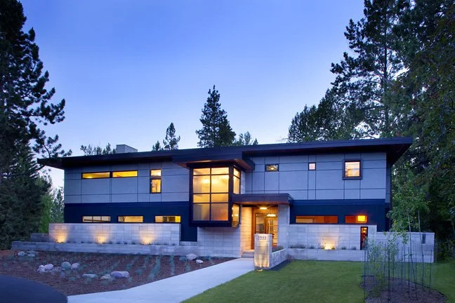 Modern two-story house with large windows, surrounded by trees, during twilight. Custom Home built in Montana by Edgell Building.