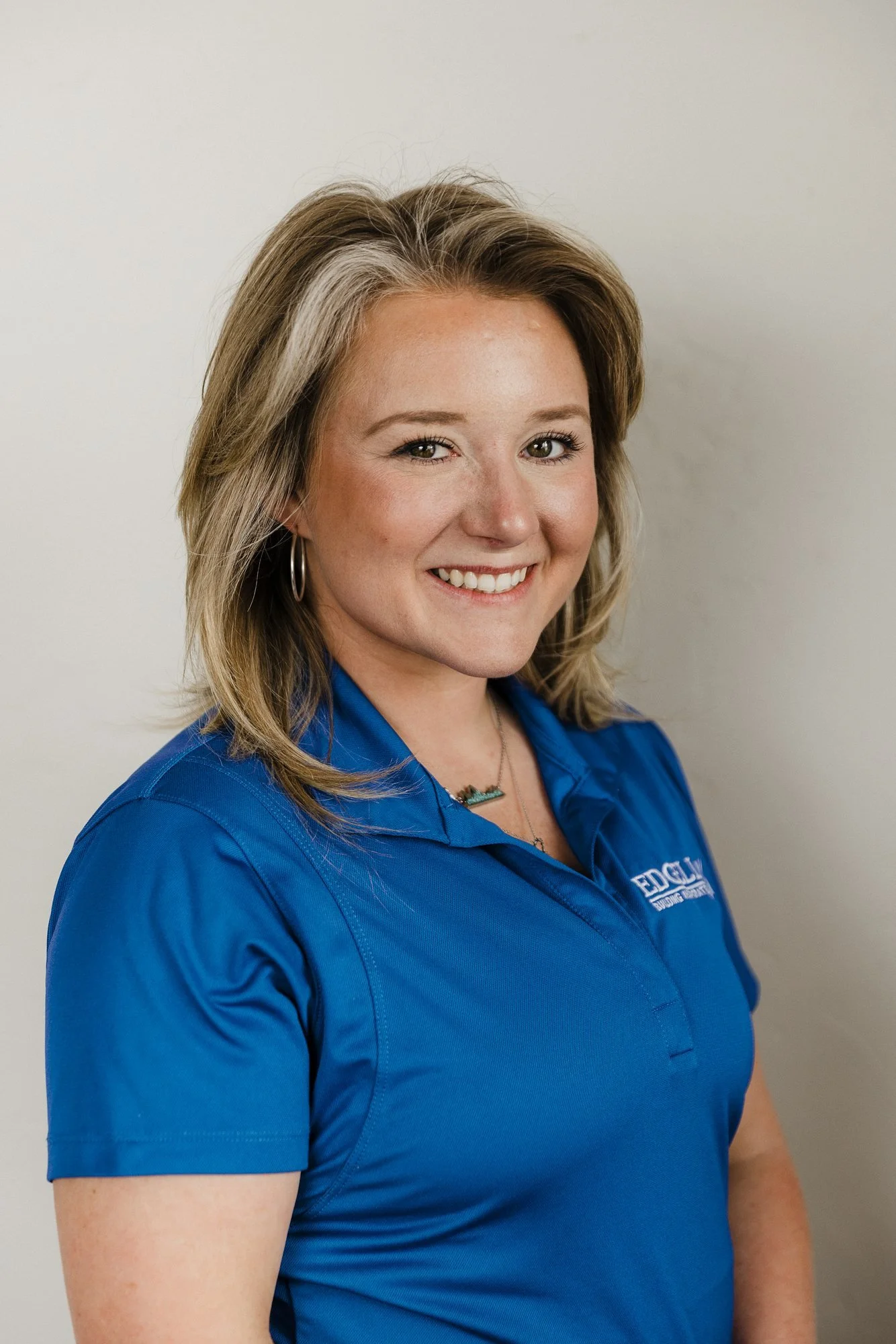 Madison Oakes of Edgell Building. A smiling woman with shoulder-length blonde hair and hoop earrings, wearing a blue Edgell polo against a plain light background.