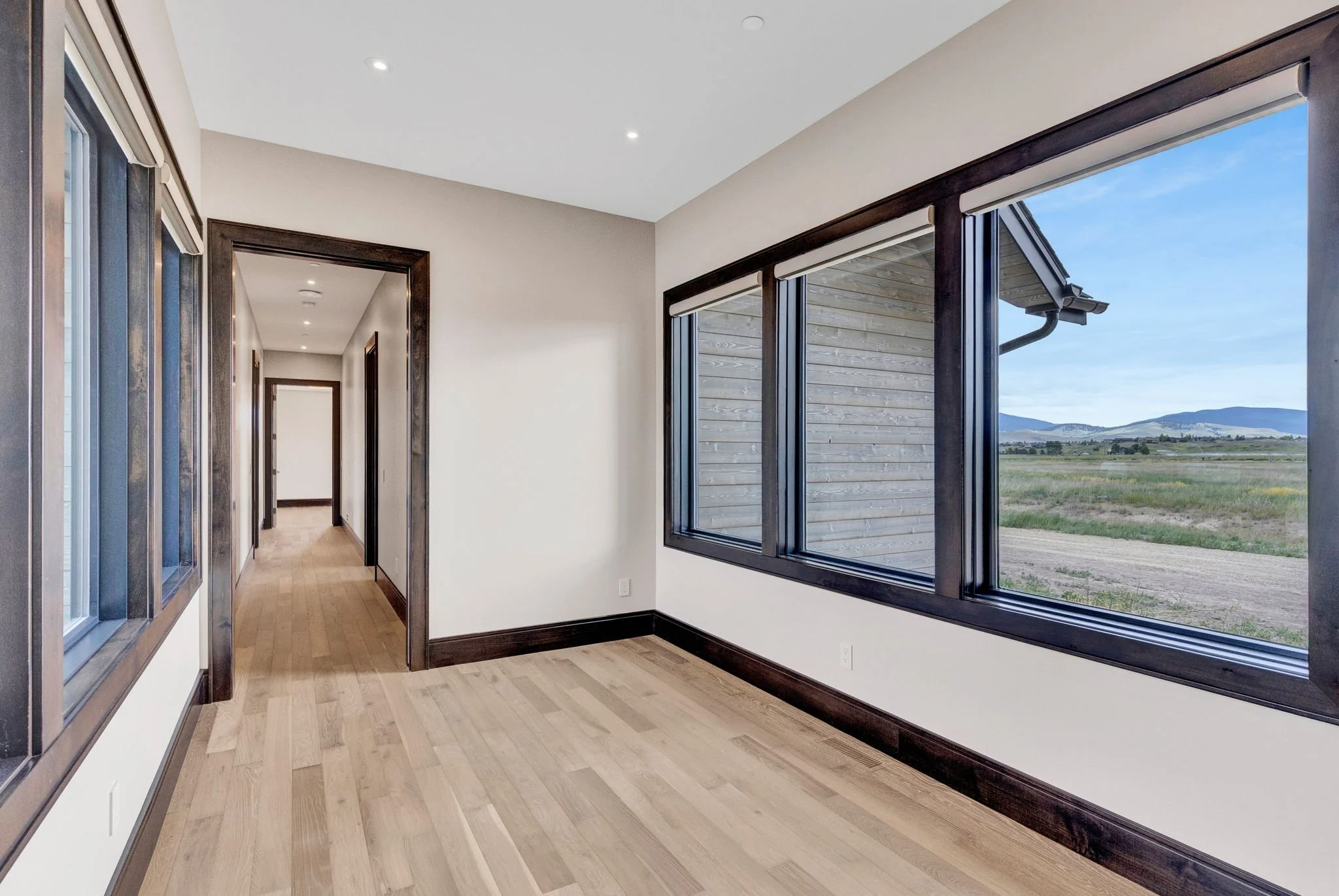 Empty room with hardwood floors, white walls, dark wood trim, large window showing an outdoor landscape with mountains Custom Home built in Montana by Edgell Building.