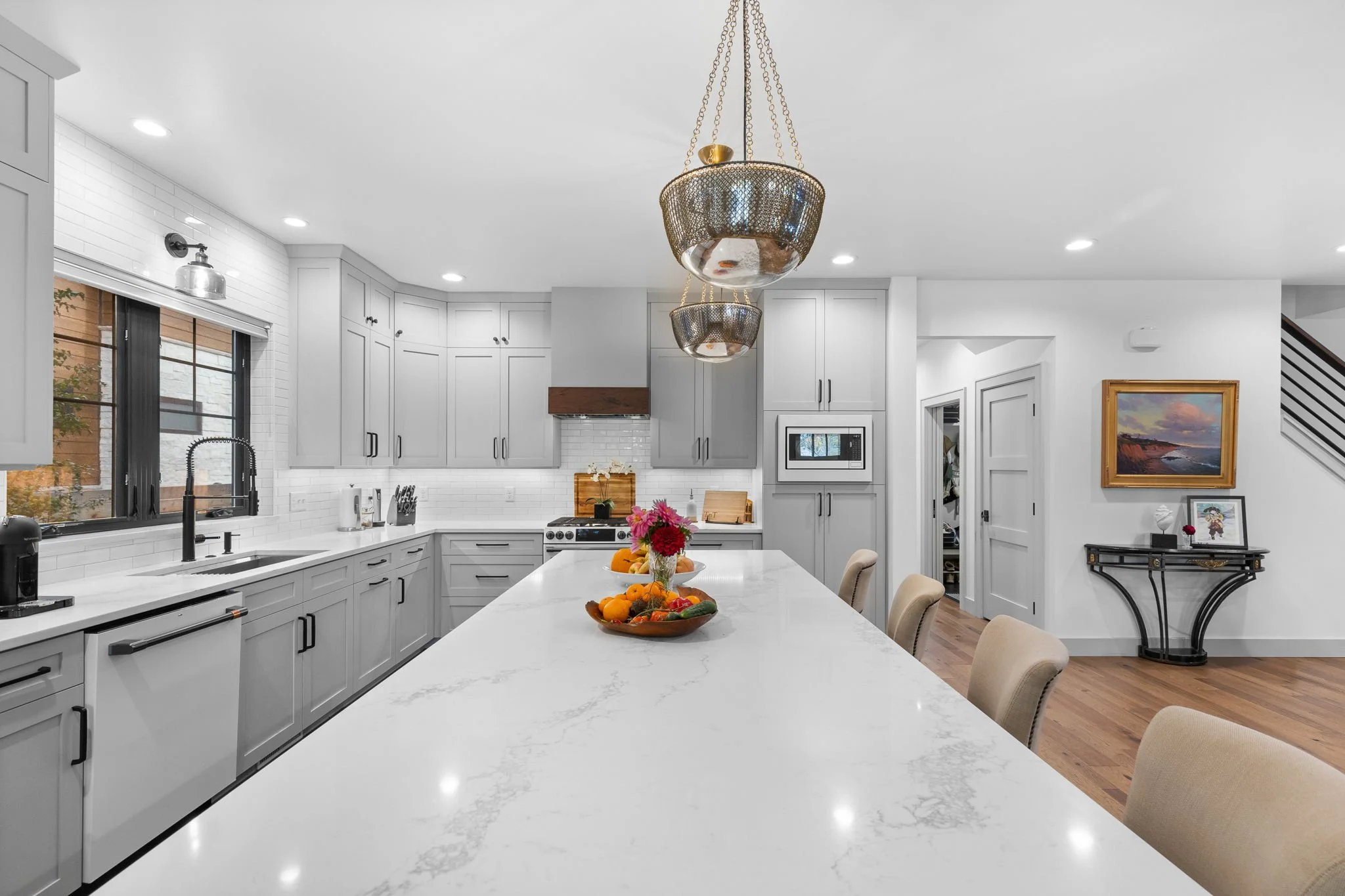 Modern kitchen with white marble island, gray cabinets, black hardware, and stainless steel appliances, illuminated by gold pendant lights. Custom Home built in Montana by Edgell Building.