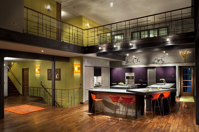 Modern kitchen with purple walls, white countertops, orange barstools, and a staircase leading to a second floor with a black railing. Custom Home built in Montana by Edgell Building.