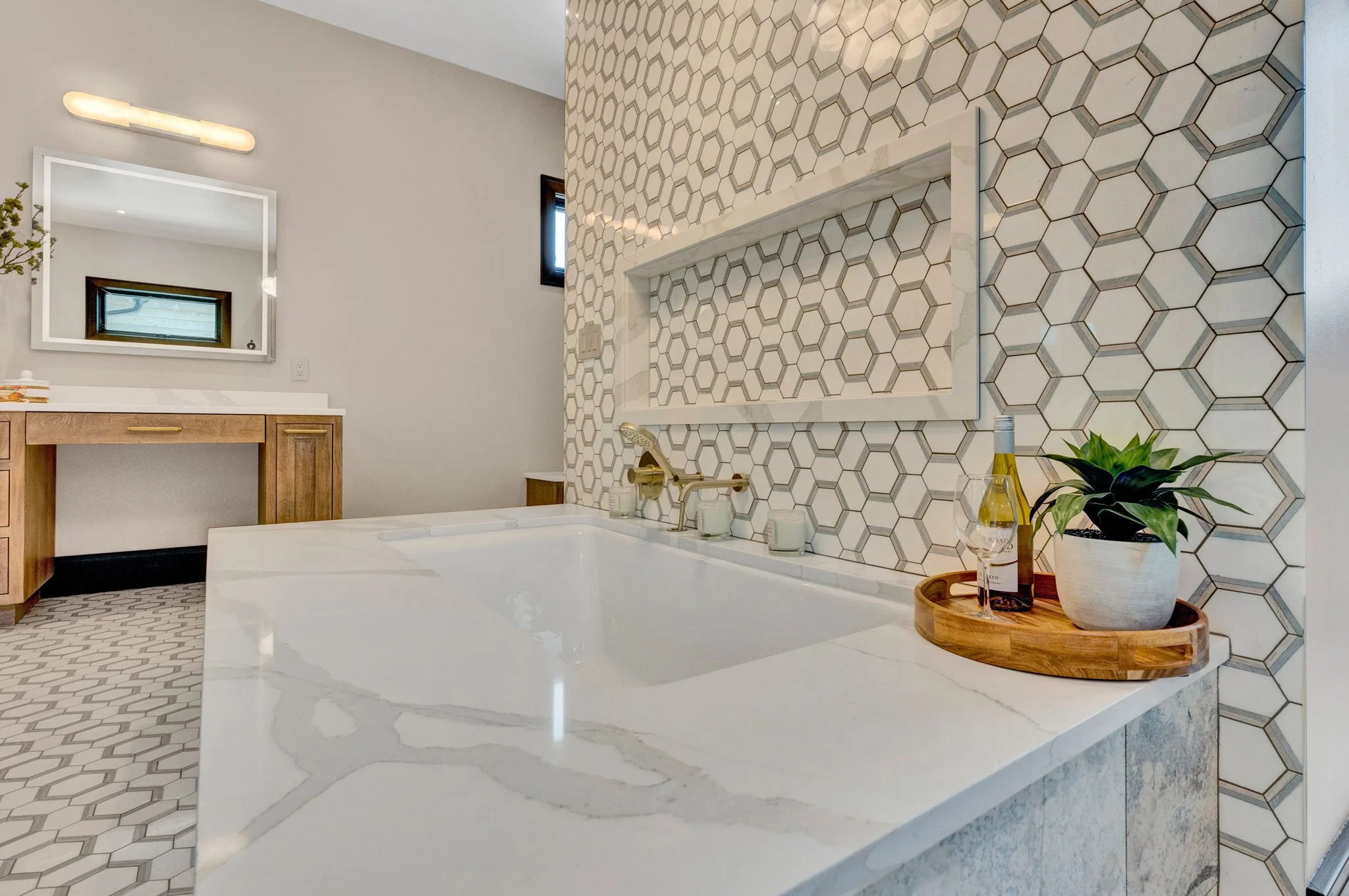 Modern bathroom with a white soaking tub, geometric honeycomb tiles, wooden vanity, and a mirror. Custom Home built in Montana by Edgell Building.