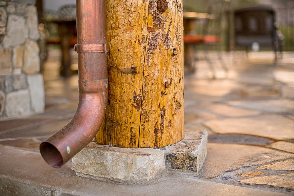 Close-up of a rusted metal downspout attached to a wooden post on a stone patio. Custom Home built in Montana by Edgell Building.