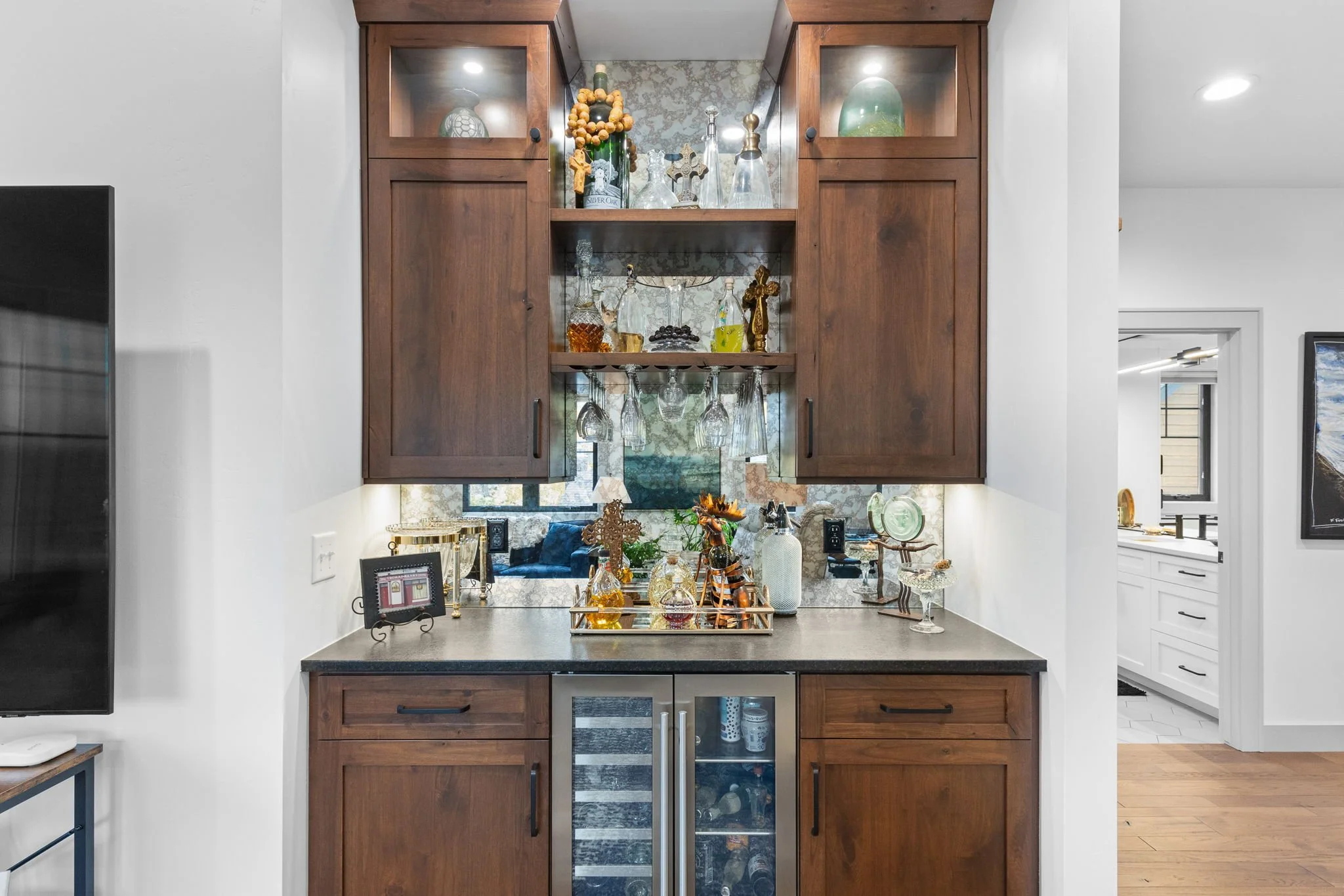 A built-in bar with dark wood cabinets, glassware, and decorative bottles, against a reflective tile backsplash. Custom Home built in Montana by Edgell Building.