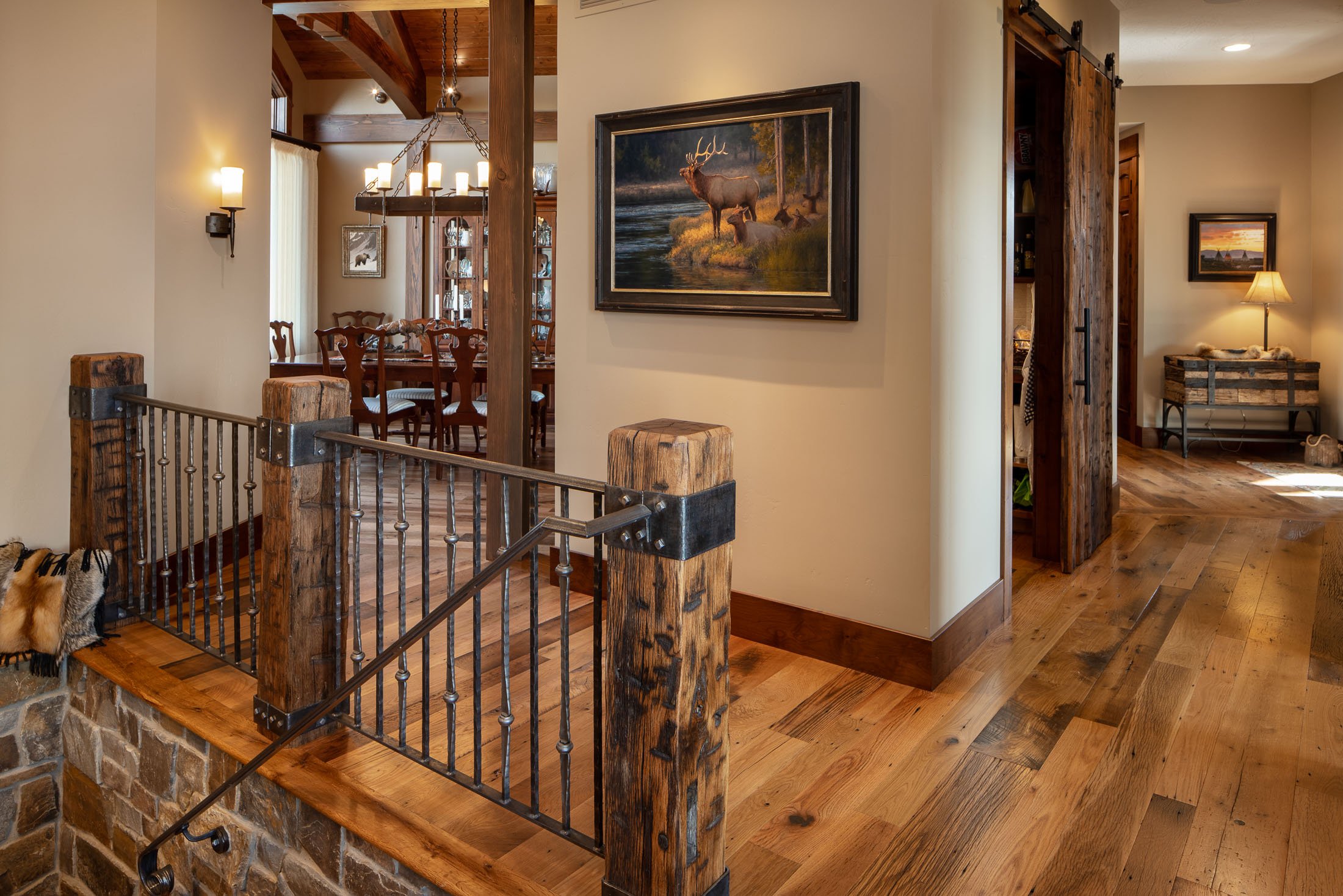 Interior of a rustic home with wood flooring, a wooden beam, a painting of a wildlife scene, and a staircase with a wooden post and metal railing. Custom Home built in Montana by Edgell Building.