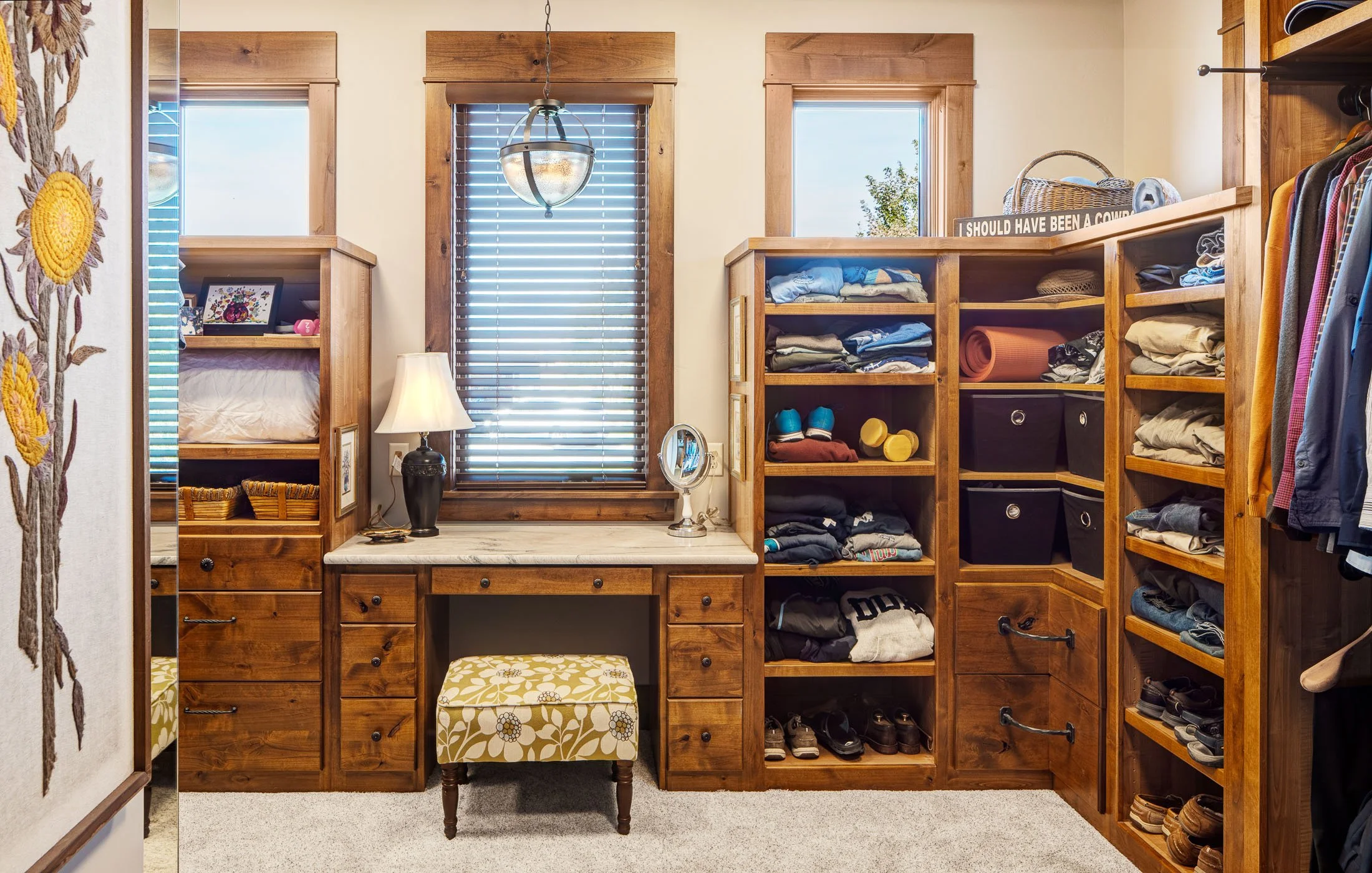 A walk-in closet with wooden shelving and a marble top vanity area, a small upholstered stool, and various folded clothes, shoes, and storage bins. Custom Home built in Montana by Edgell Building.