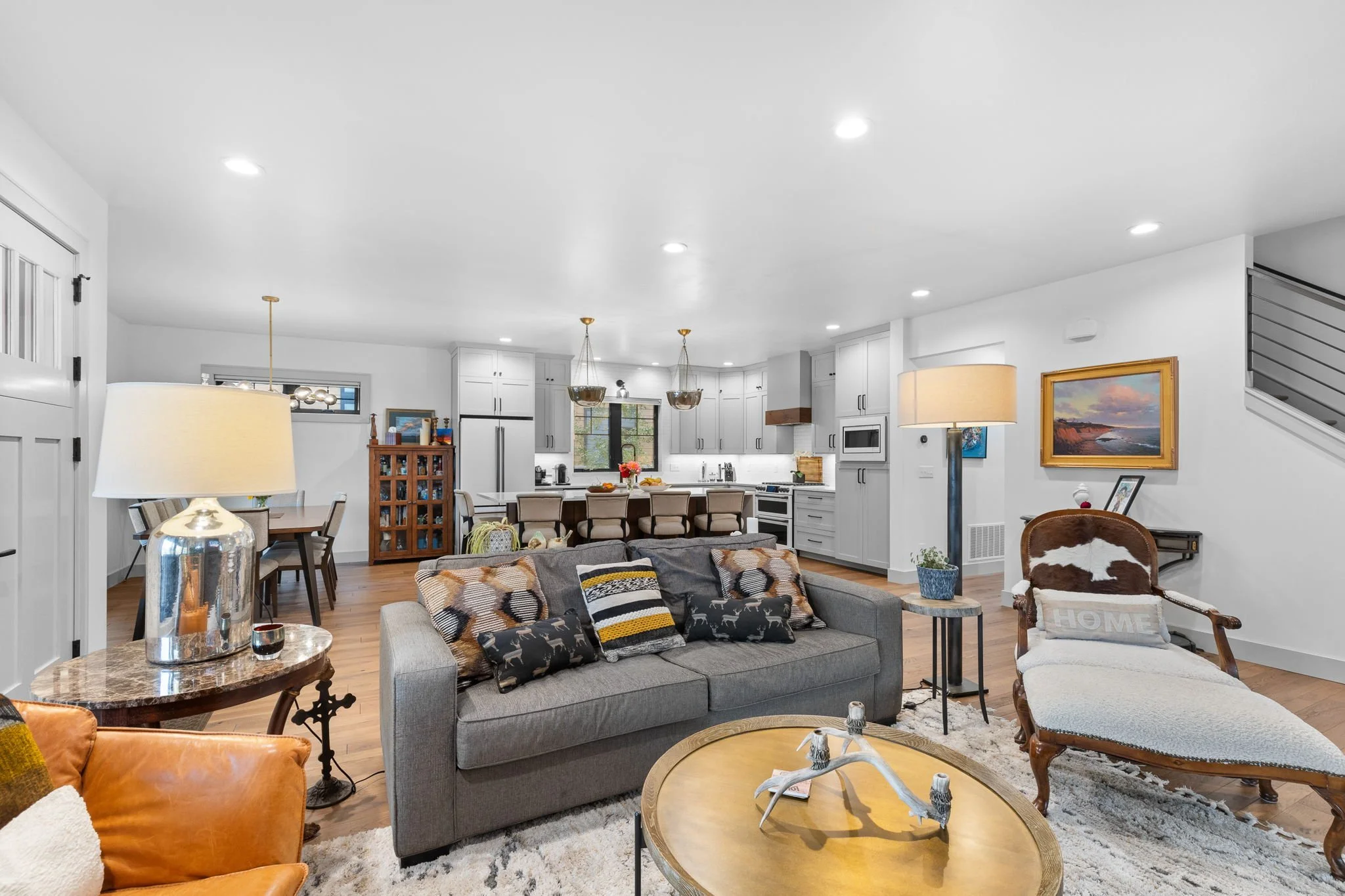 Open-concept living area with gray sofa, upholstered chaise lounge, wooden coffee table, and decorative pillows, with a view into a bright white kitchen. Custom Home built in Montana by Edgell Building.