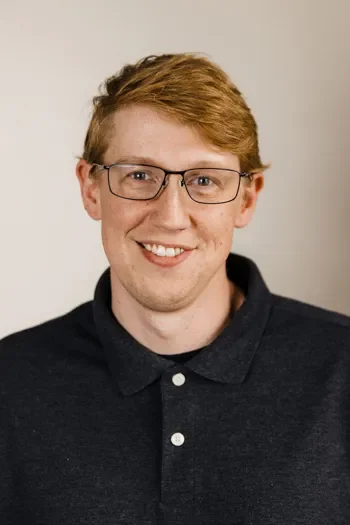 Jacob Dransfield of Edgell Building. A young man with glasses, red hair, and a smile, wearing a black collared shirt against a plain background.