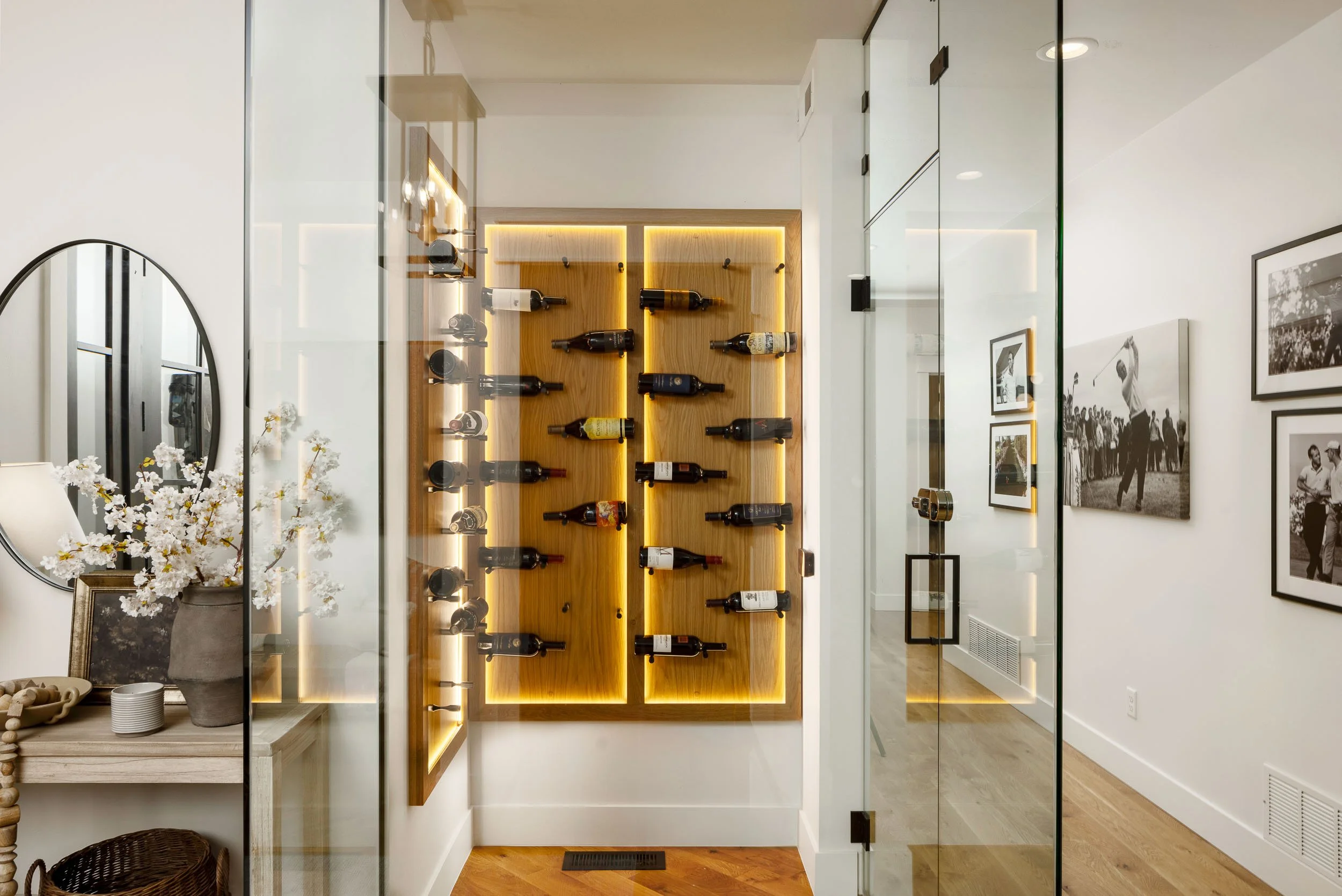 Interior view of a modern home, showcasing a glass door, a wall-mounted wine rack with bottles, and black-and-white photographs on the walls. Home Designed and Built By Edgell Building in Western Montana.