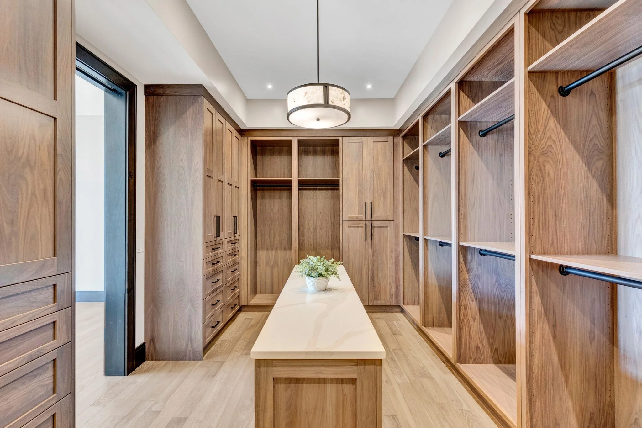 A spacious walk-in closet with wooden built-in cabinets and shelves, a central island with a plant, and a ceiling light fixture. Custom Home built in Montana by Edgell Building.
