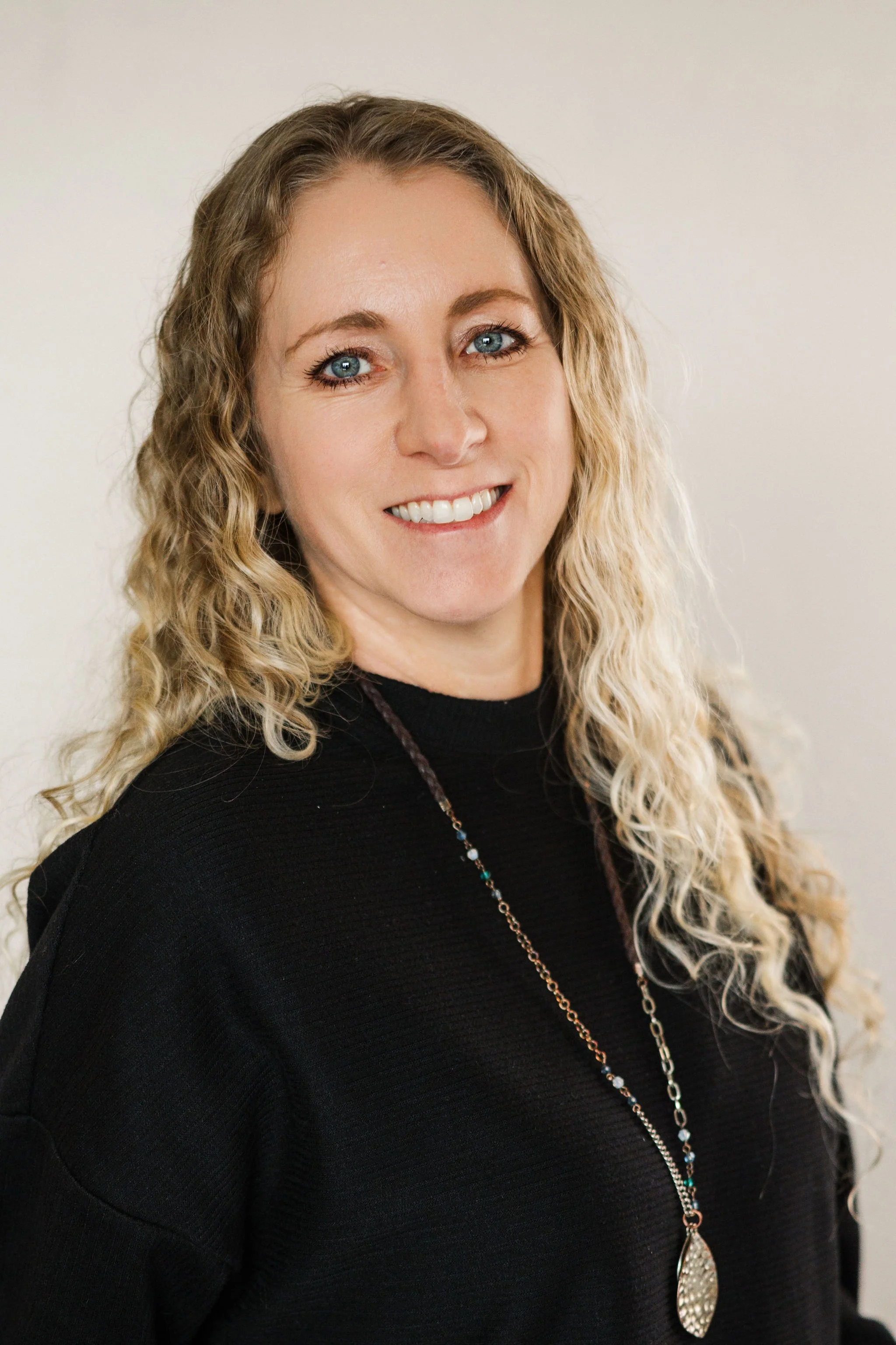 Amber Robinson of Edgell Building. A woman with curly blonde hair, wearing a black top and a long beaded necklace, smiling at the camera against a plain light background.
