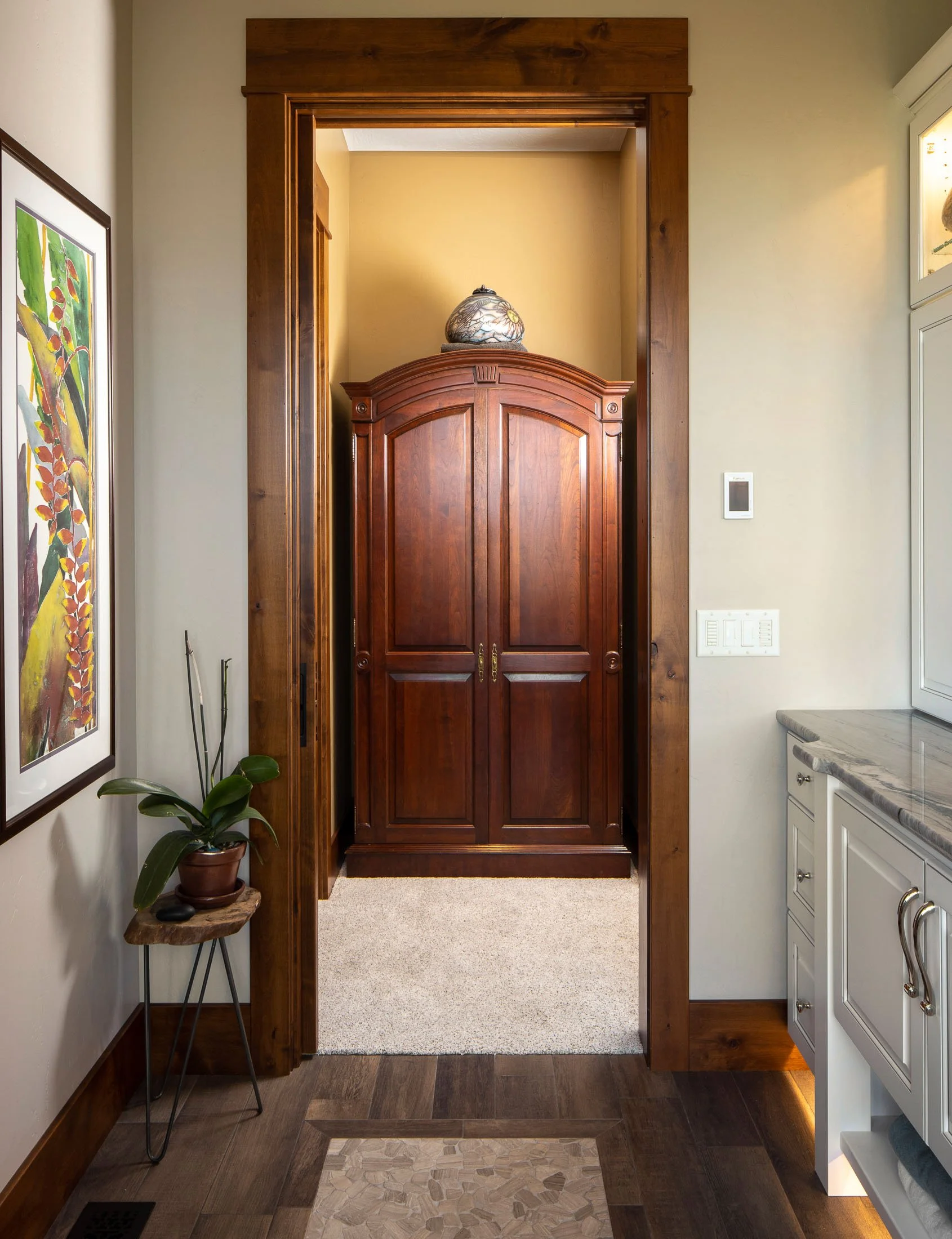 A wooden cabinet or wardrobe in a small niche, topped with a decorative ceramic vase, with hardwood flooring and a small carpet. Custom Home built in Montana by Edgell Building.