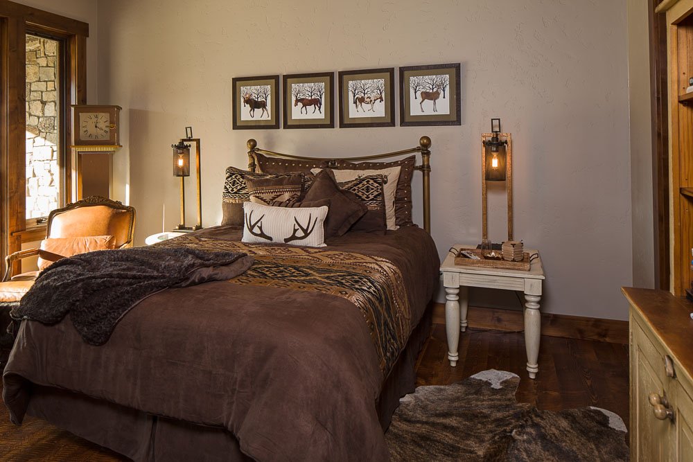 A cozy bedroom with a brown bedspread, decorative pillows, and wall art of moose, featuring rustic decor, wood accents, and warm lighting. Custom Home built in Montana by Edgell Building.