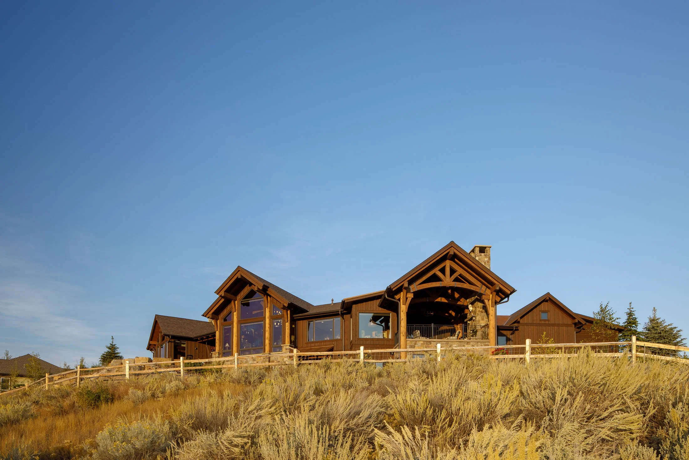 A large wooden house on a hill with a clear blue sky in the background. Custom Home built in Montana by Edgell Building.