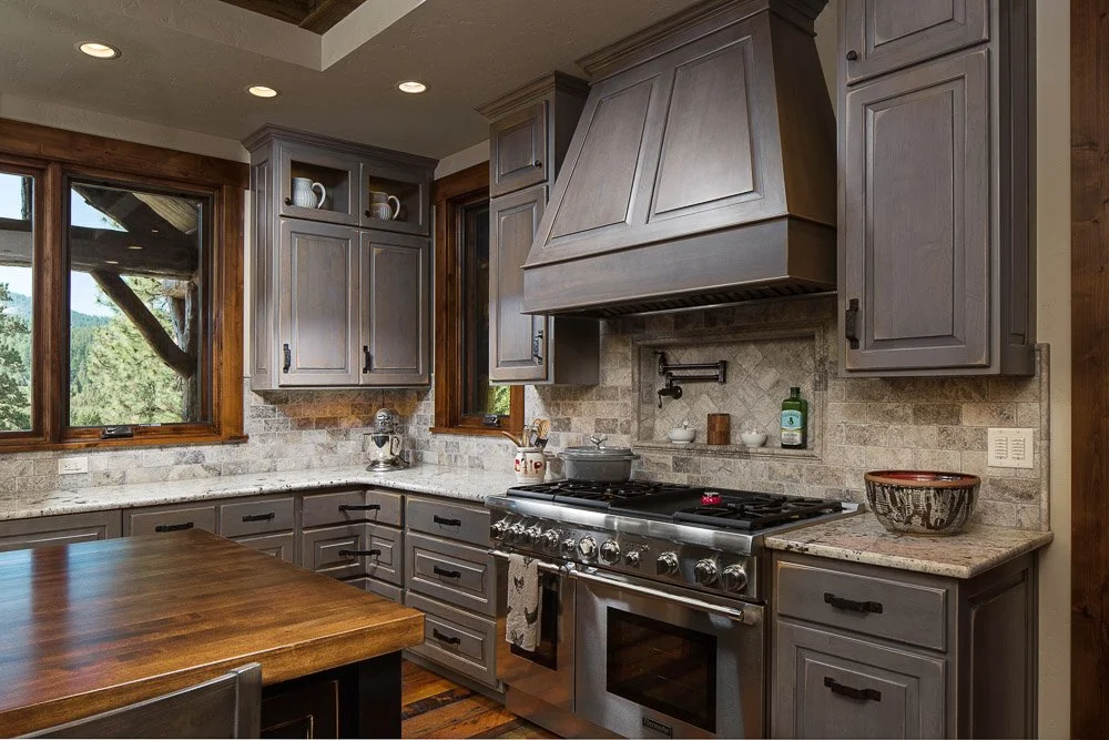 Kitchen with gray cabinets, granite countertops, a stove, and two large windows. Custom Home built in Montana by Edgell Building.
