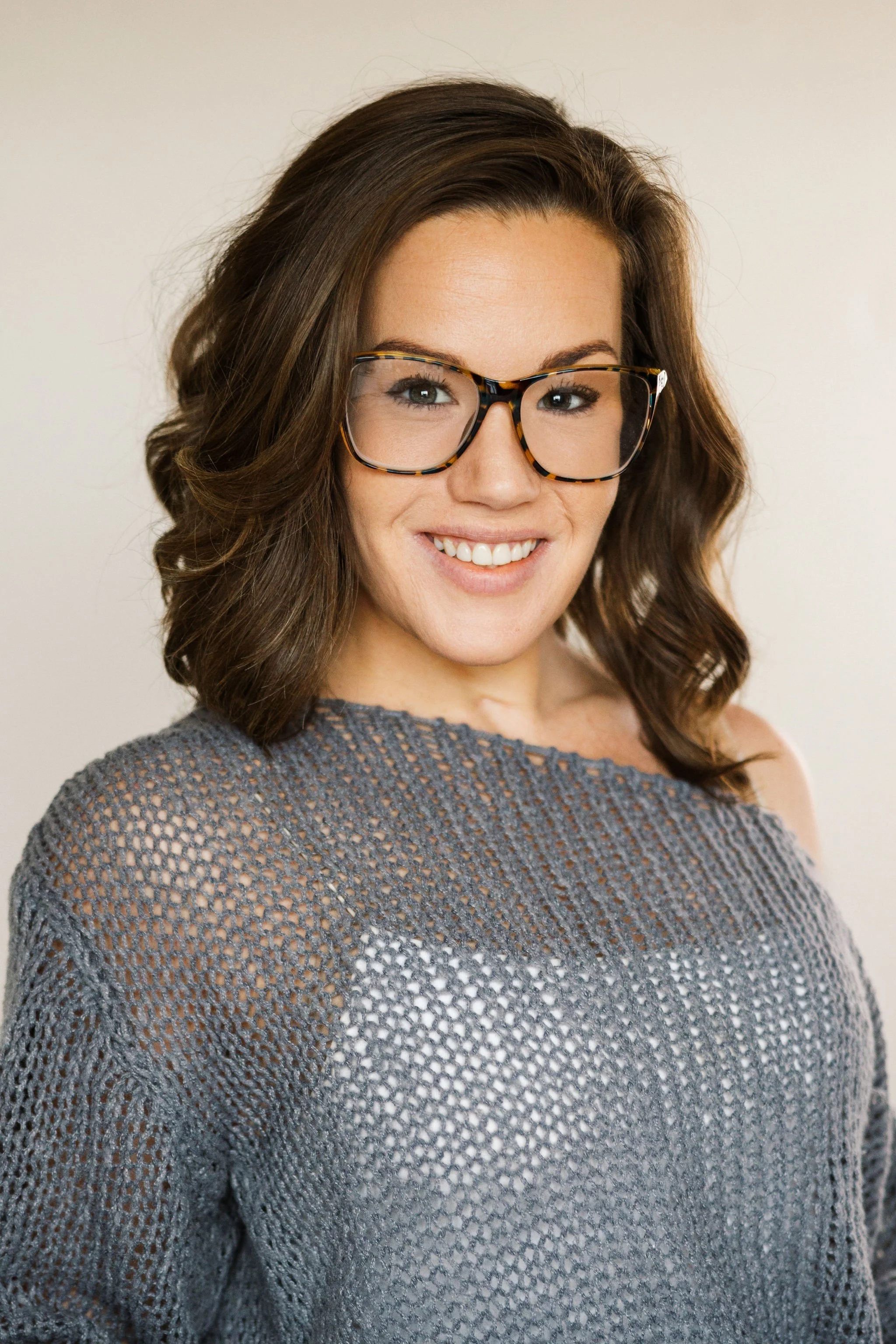 MacKenzie Lemcke of Edgell Building. A woman with shoulder-length, wavy brown hair and glasses, smiling, wearing a gray mesh sweater against a plain light background.