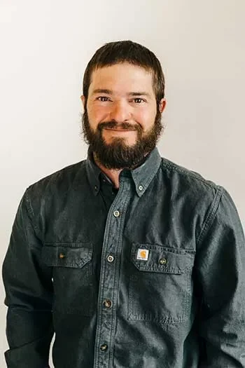 Robbie Barreiros of Edgell Building. A man with dark hair and a beard smiling, wearing a dark gray button-up shirt, standing against a plain white wall.