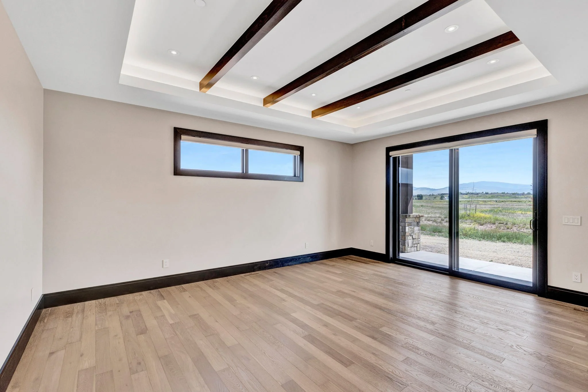 Empty living room with hardwood floors, white walls, large glass sliding door to the outside, and rectangular windows near the ceiling, in a modern house with a scenic view of fields and mountains. Custom Home built in Montana by Edgell Building.