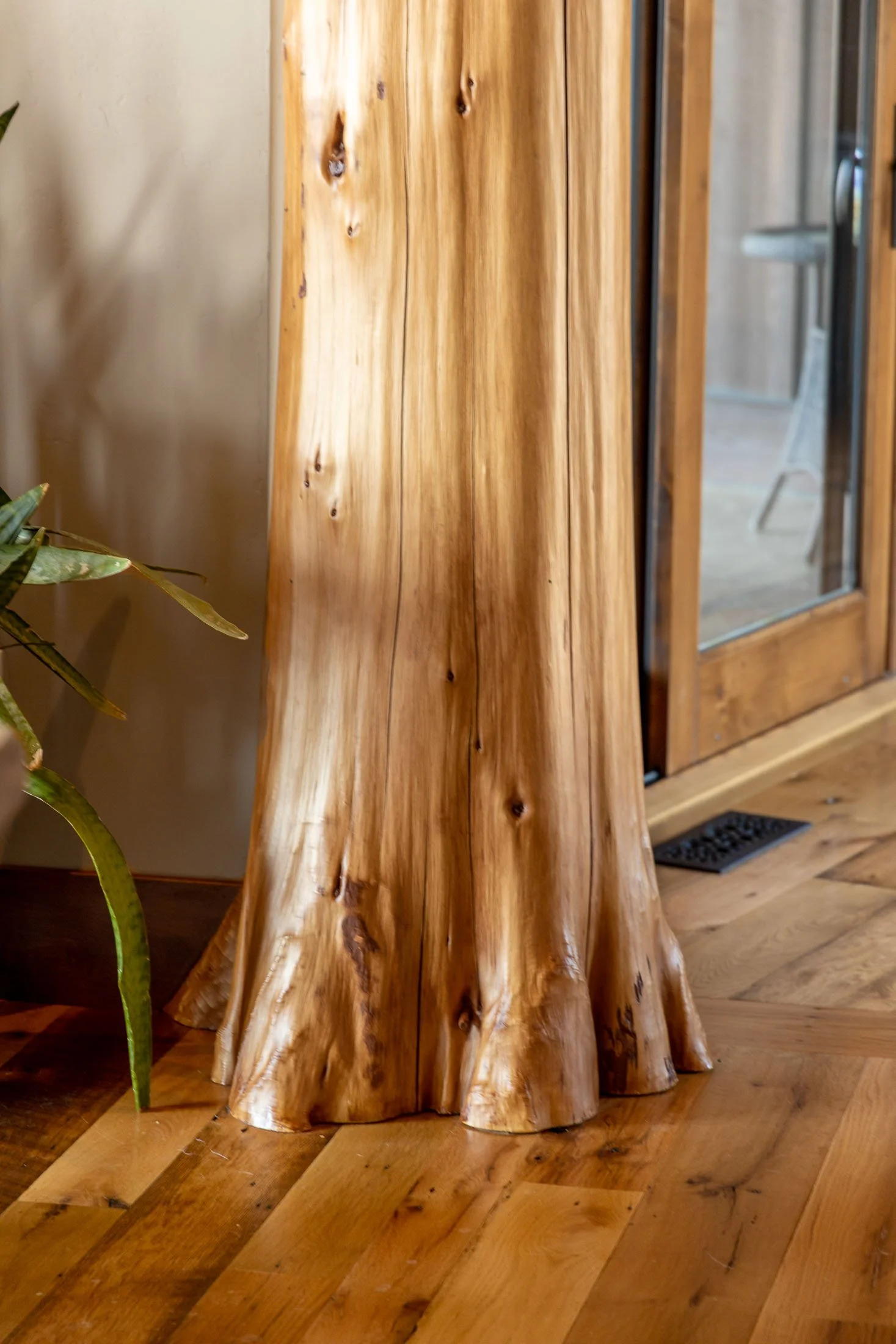 Close-up of a wooden salon with a tree trunk base supporting a counter or table, situated indoors on a wooden floor near a glass door and a vent. Custom Home built in Montana by Edgell Building.