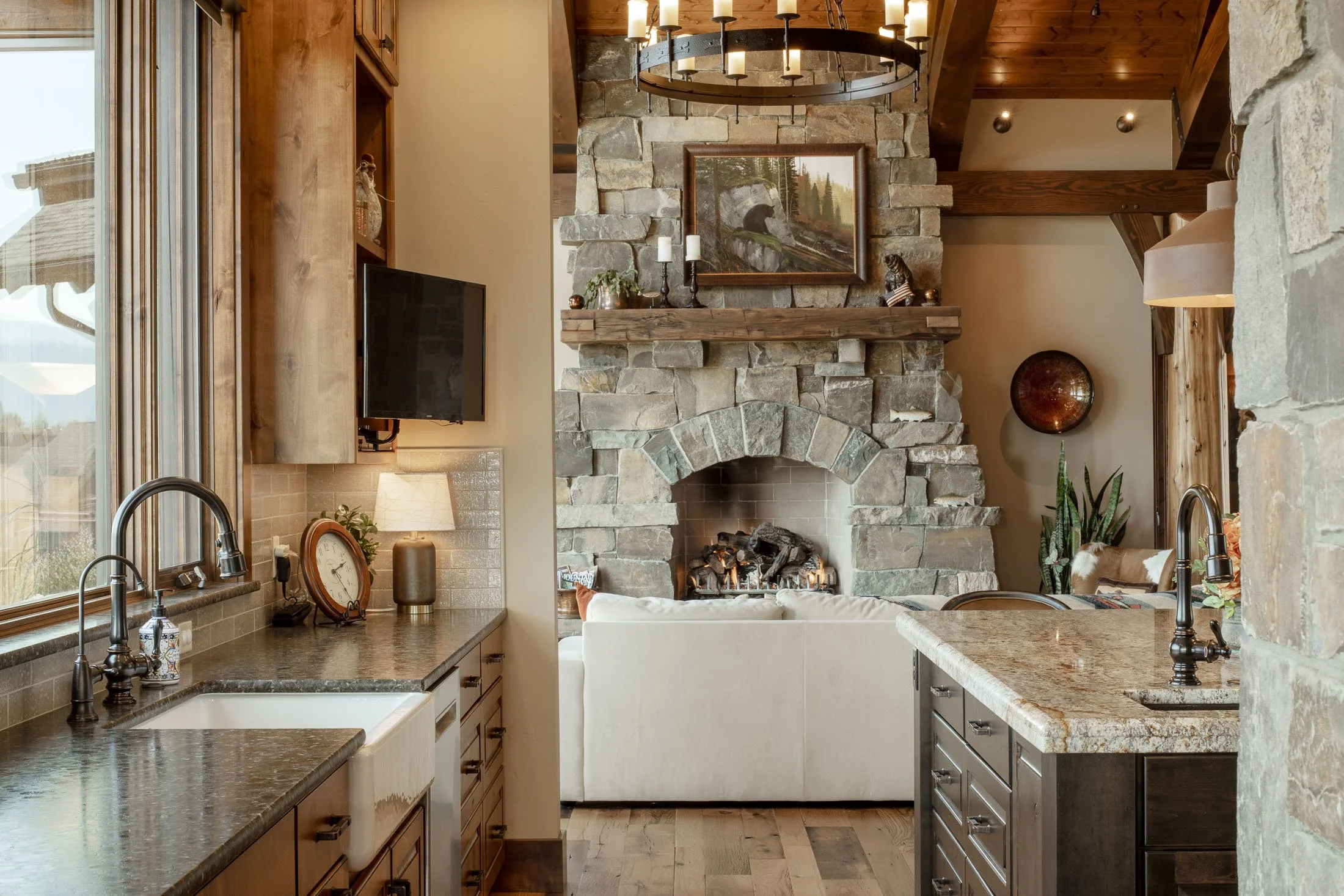 Living room with stone fireplace, white sofa, wooden accents, and kitchen counters visible in the foreground. Custom Home built in Montana by Edgell Building.