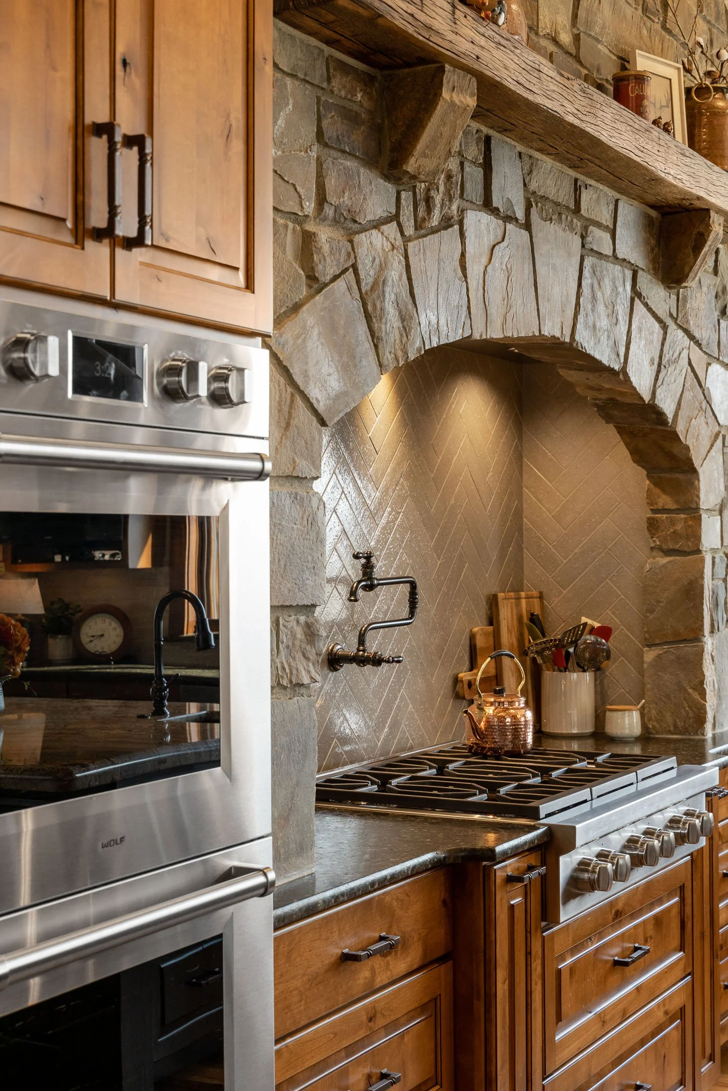 A rustic kitchen with a stone archway and backsplash, wooden cabinets, and stainless steel appliances. Custom Home built in Montana by Edgell Building.