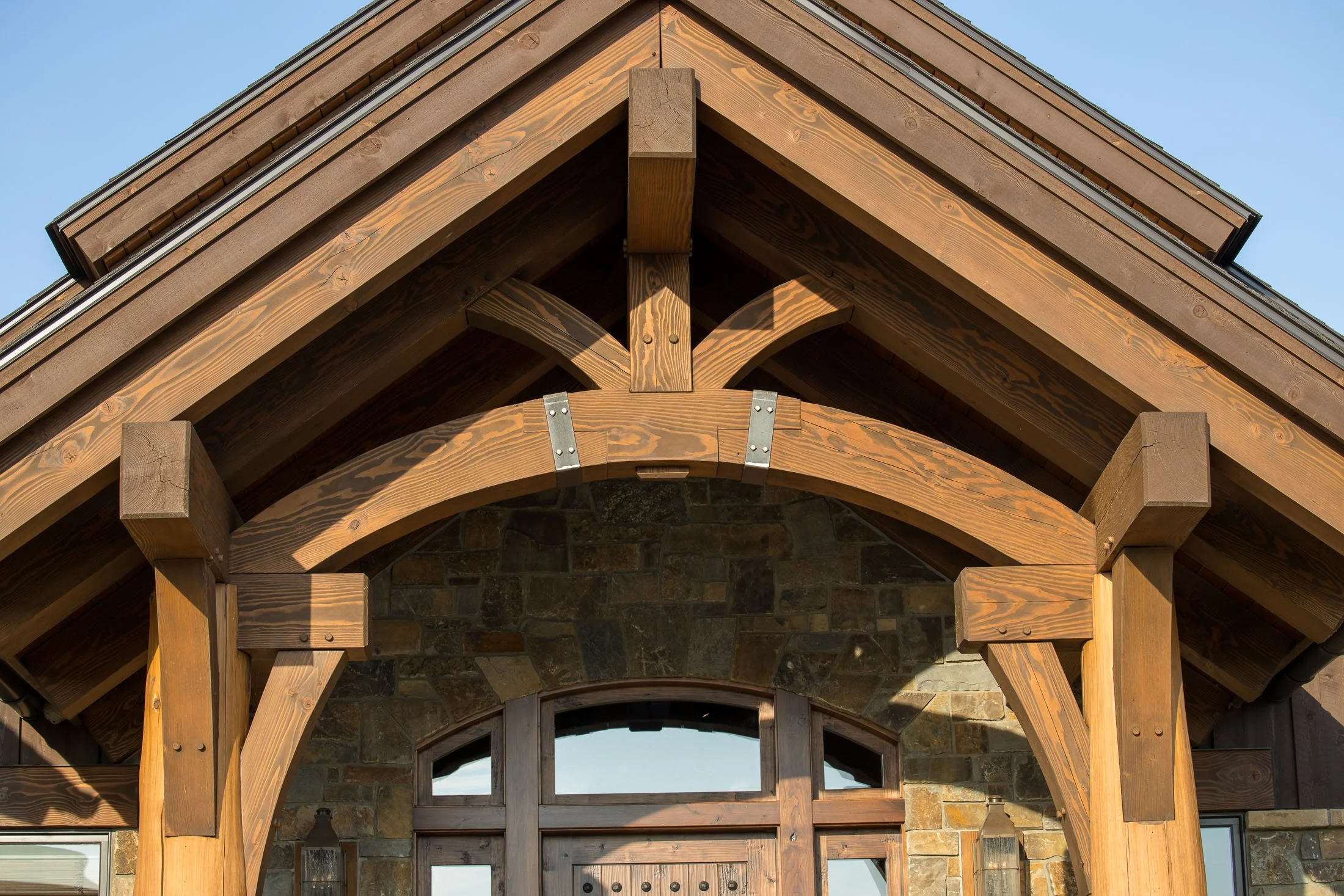 Close-up of a rustic house entrance with a wooden archway and stone walls, under a gabled roof. Custom Home built in Montana by Edgell Building.