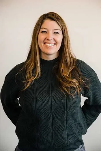 Ericka Keeler Woronik of Edgell Building. Woman with long brown hair smiling and wearing a black sweater standing against a light background.