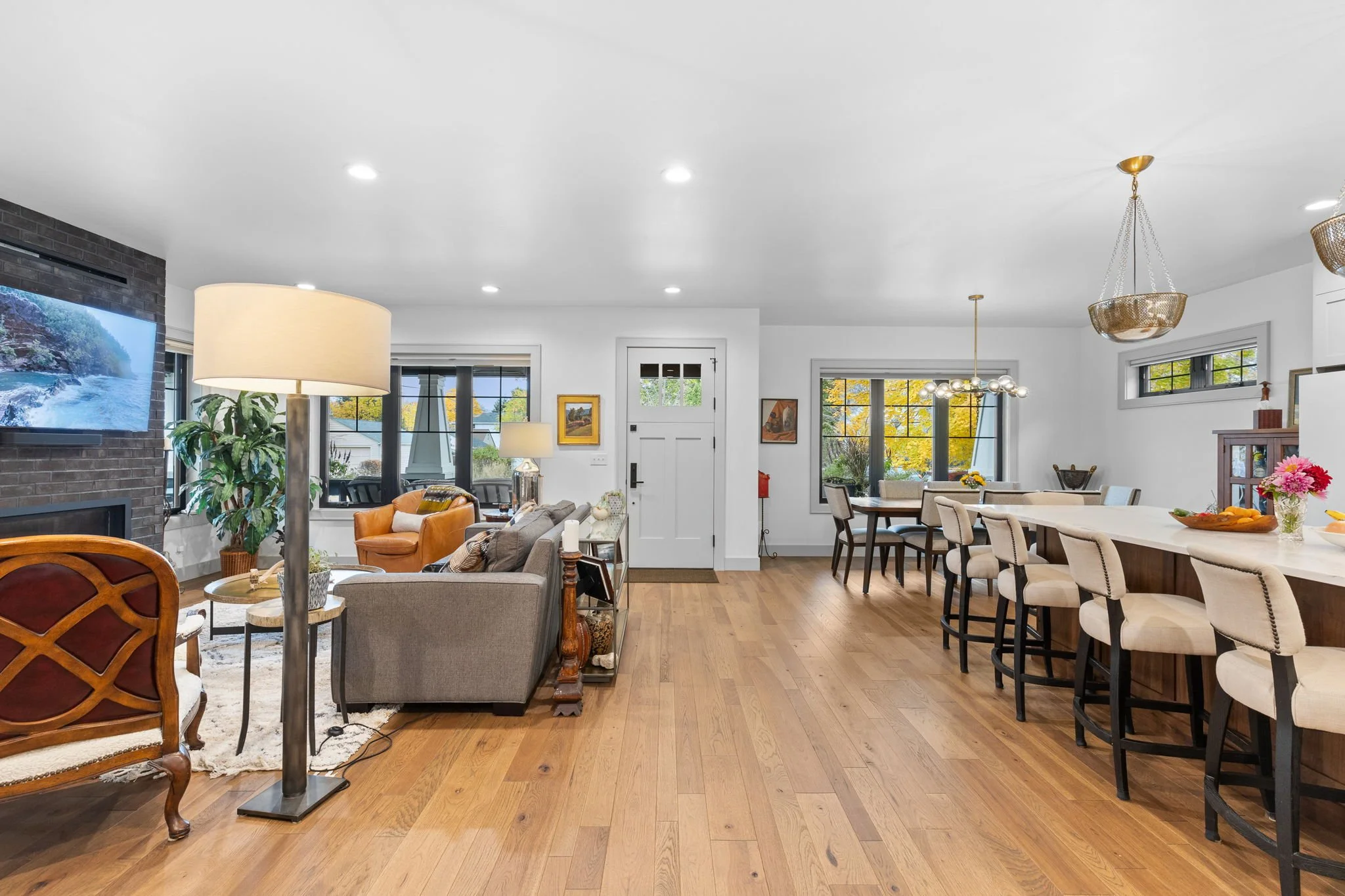Open-concept living room and kitchen with hardwood floors, white walls, various seating options, large windows, kitchen island with bar stools, and décor. Custom Home built in Montana by Edgell Building.