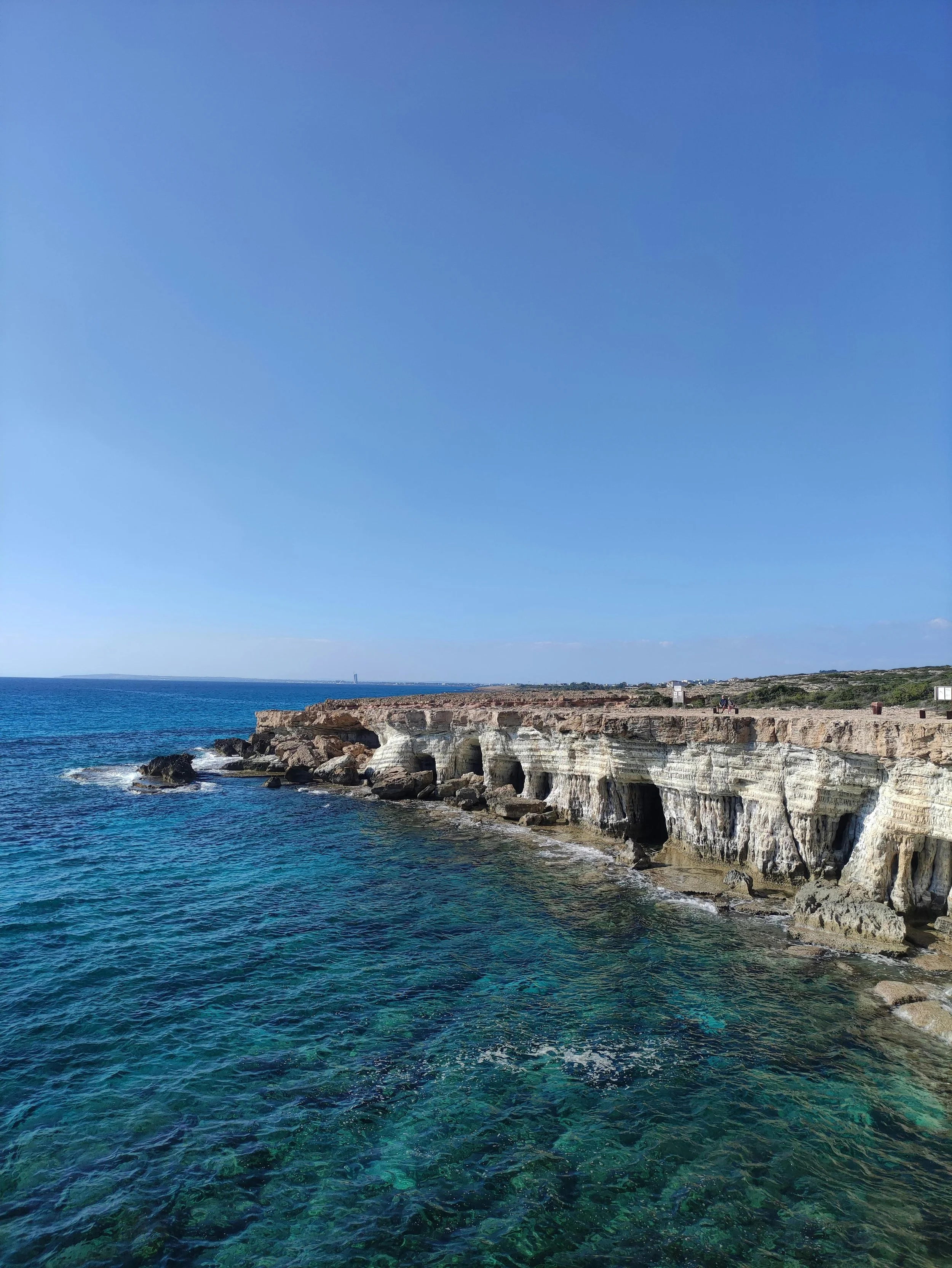 Ocean coastline with clear blue water and eroded white cliffs under a bright blue sky.