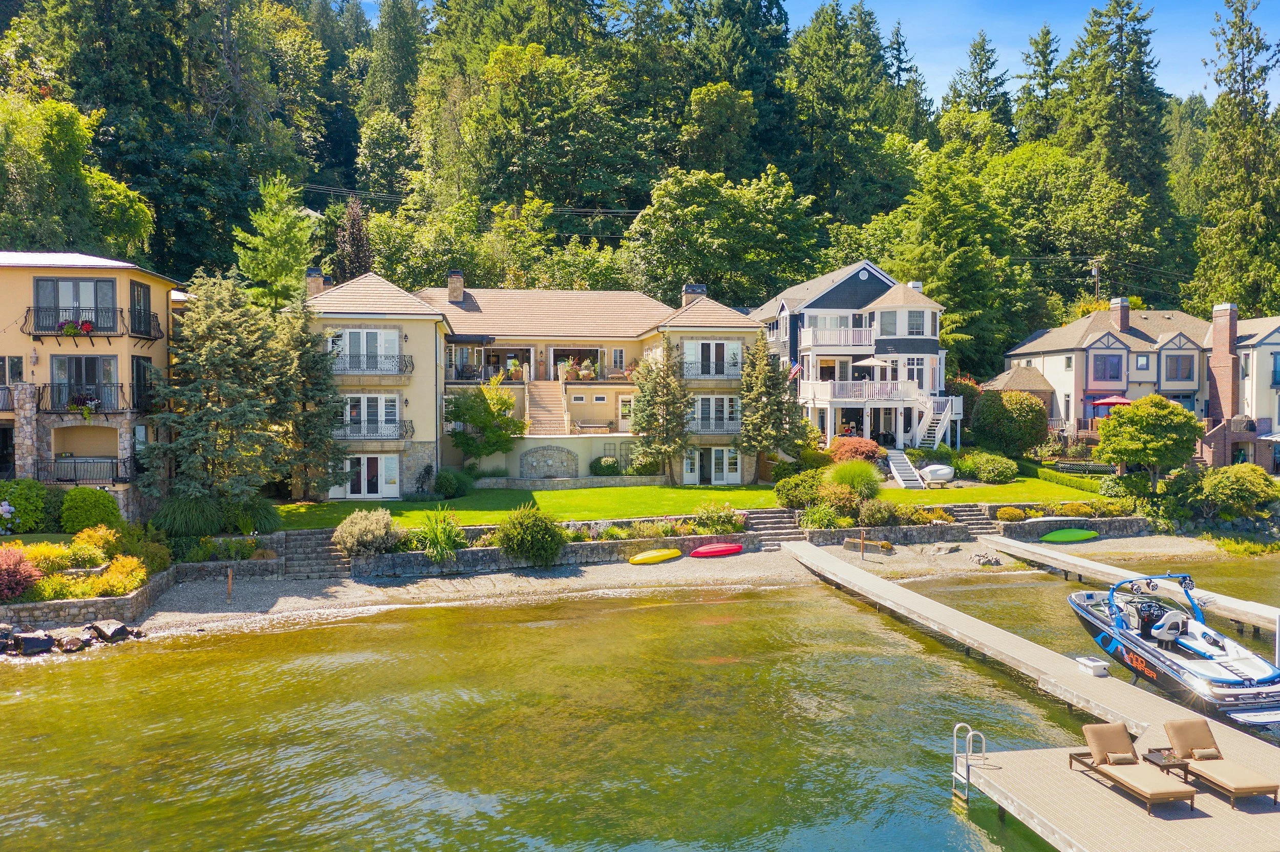 Luxury lakeside homes with lush landscaping, kayaks, and a boat docked at a waterfront deck