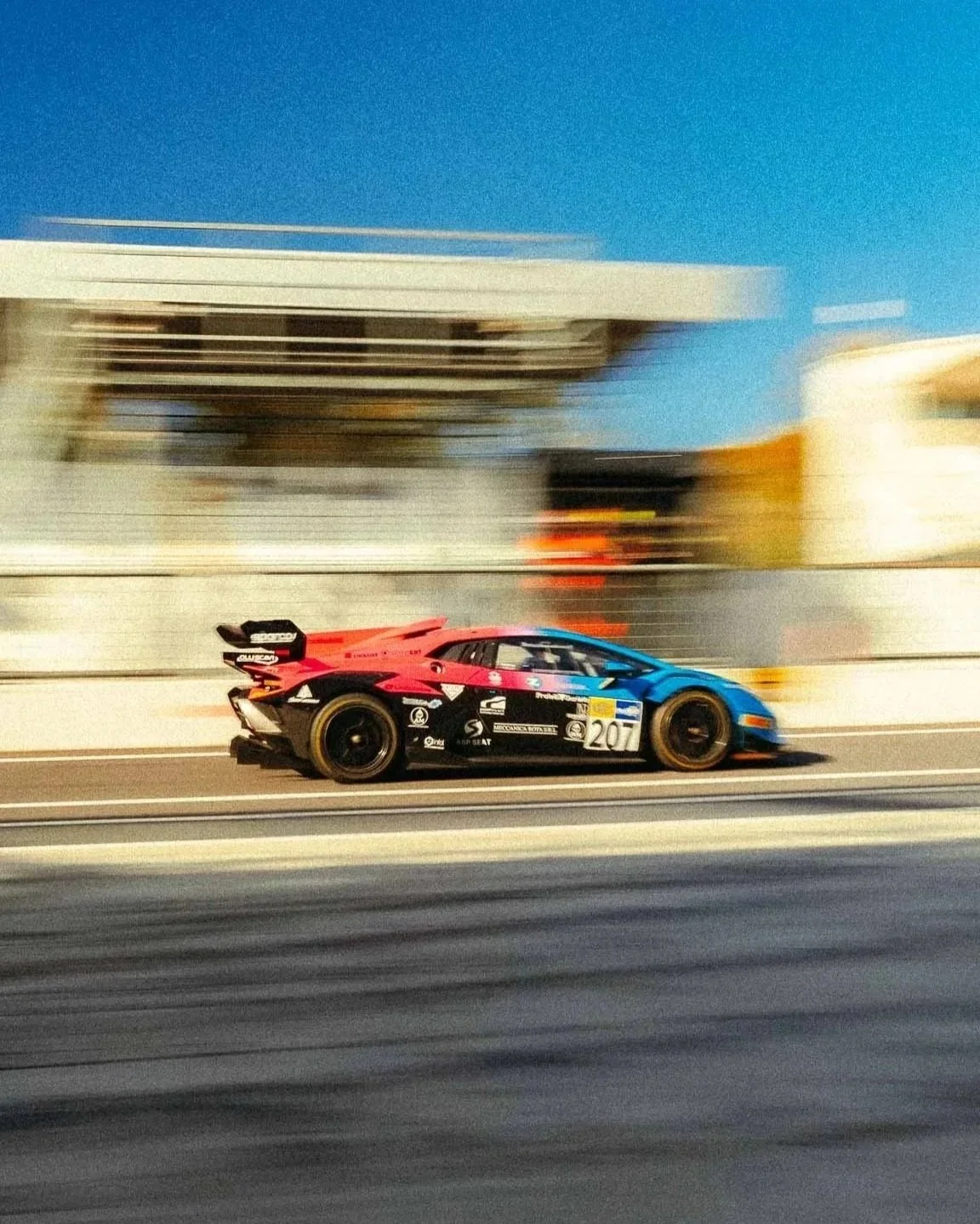 A colorful racing car speeds along a race track with motion blur in the background.
