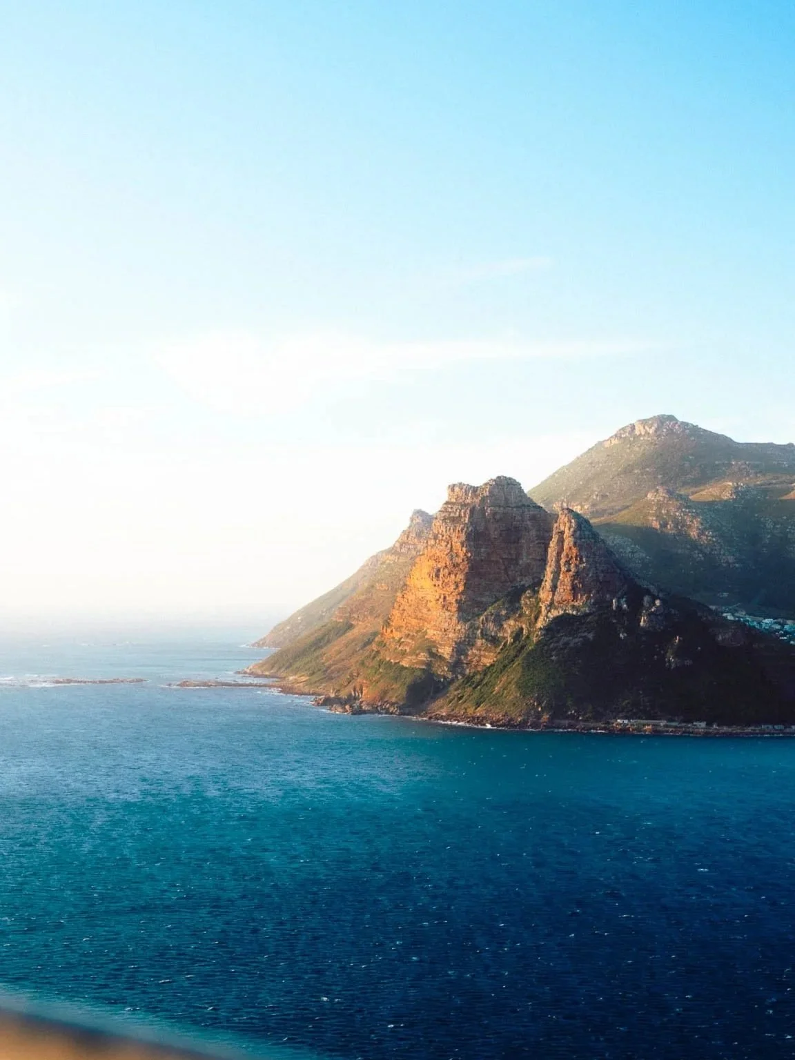 Coastal landscape with a large mountain and blue ocean water under a clear sky