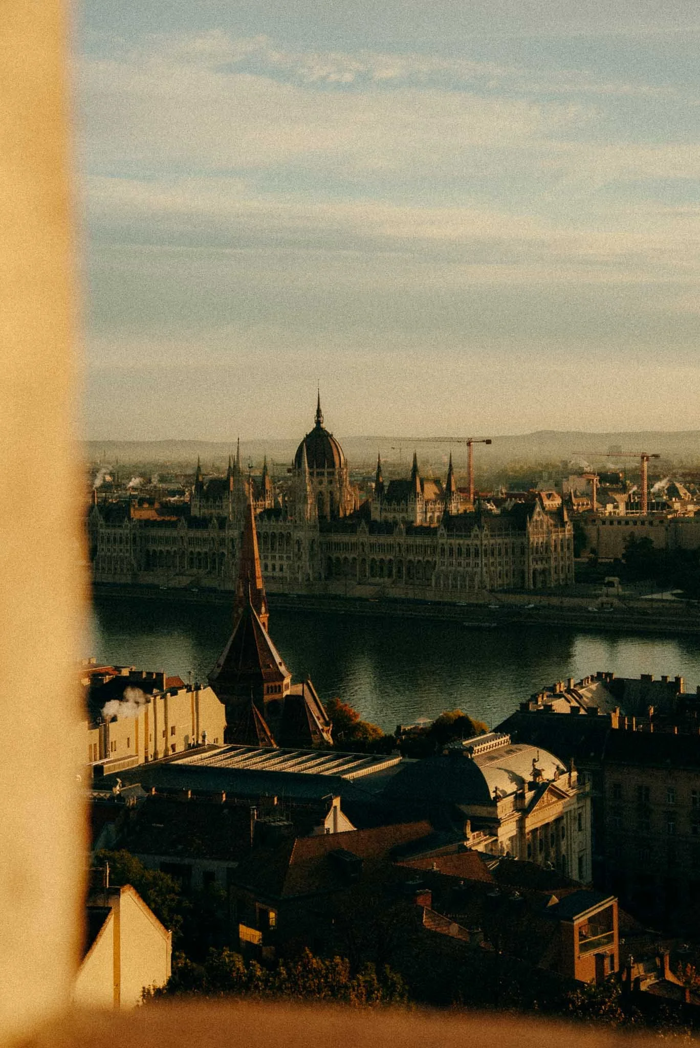 View of a historic cityscape with a large domed building, a river, and older buildings in the foreground, taken during sunset.