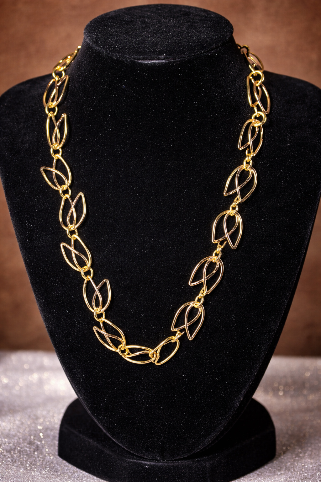 Gold chain necklace with leaf-shaped links displayed on a black velvet holder.