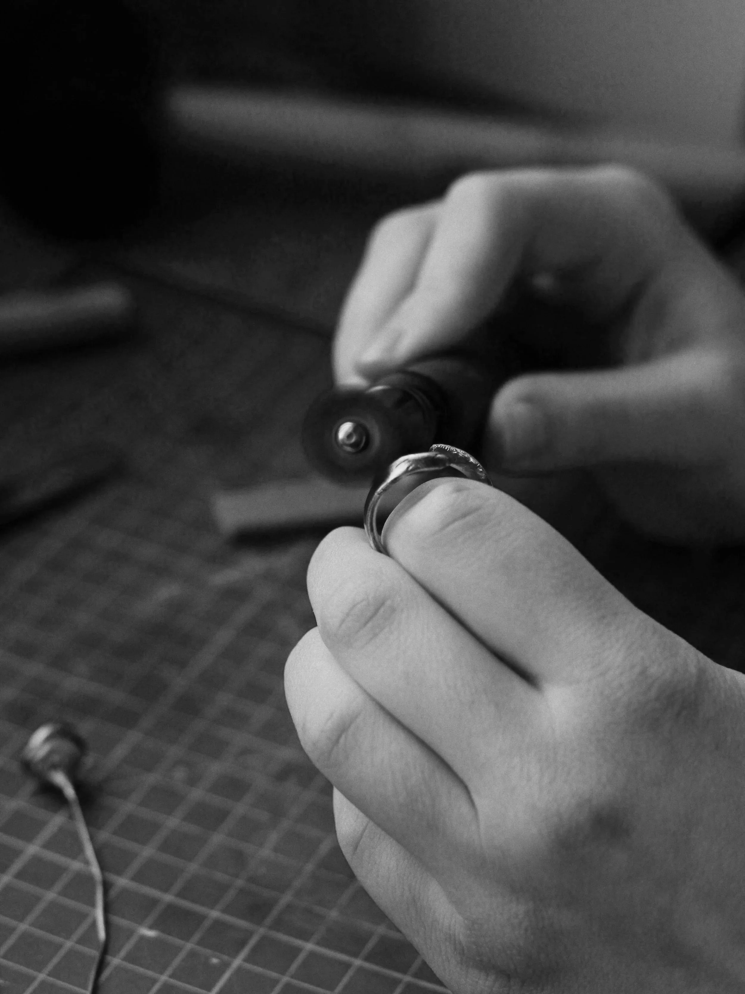 Close-up of a person’s hand holding a ring and a tool, possibly a jewelry-making or repair process, in black and white.