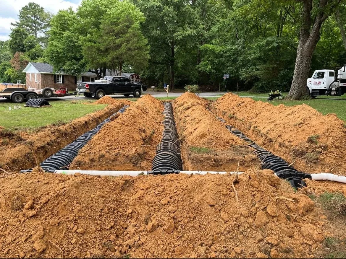 S&W Septic and Portable Services installing a new septic system and leach field in Floyd County, Georgia. This image shows the professional installation process, with new pipes laid in the trenches before being covered.