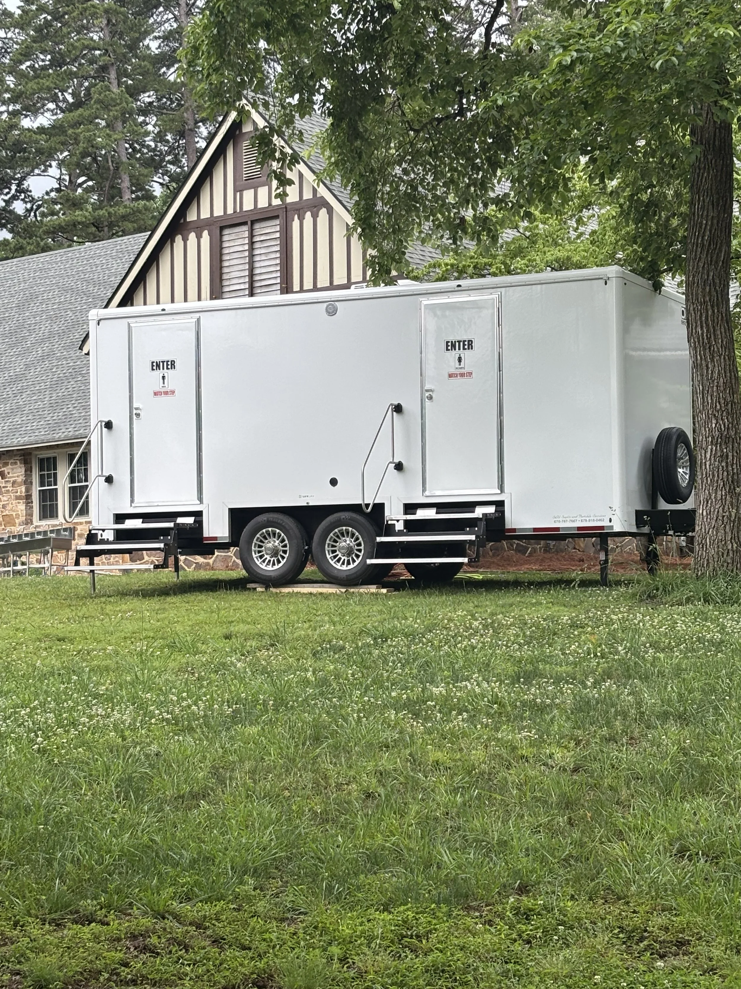 Close-up exterior view of a pristine white luxury restroom trailer rental with stairs and handrails, set up on a grassy lawn for an outdoor event by S&W Septic in Northwest Georgia.