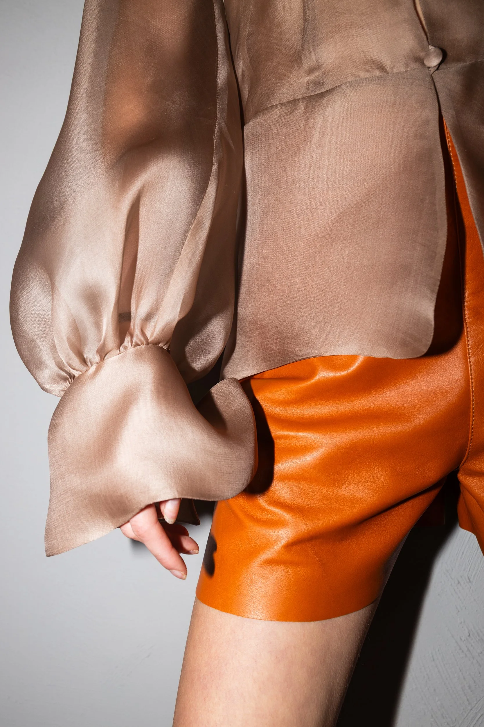 Close-up of a person wearing a shiny beige satin blouse with puffy long sleeves and an orange leather mini skirt.