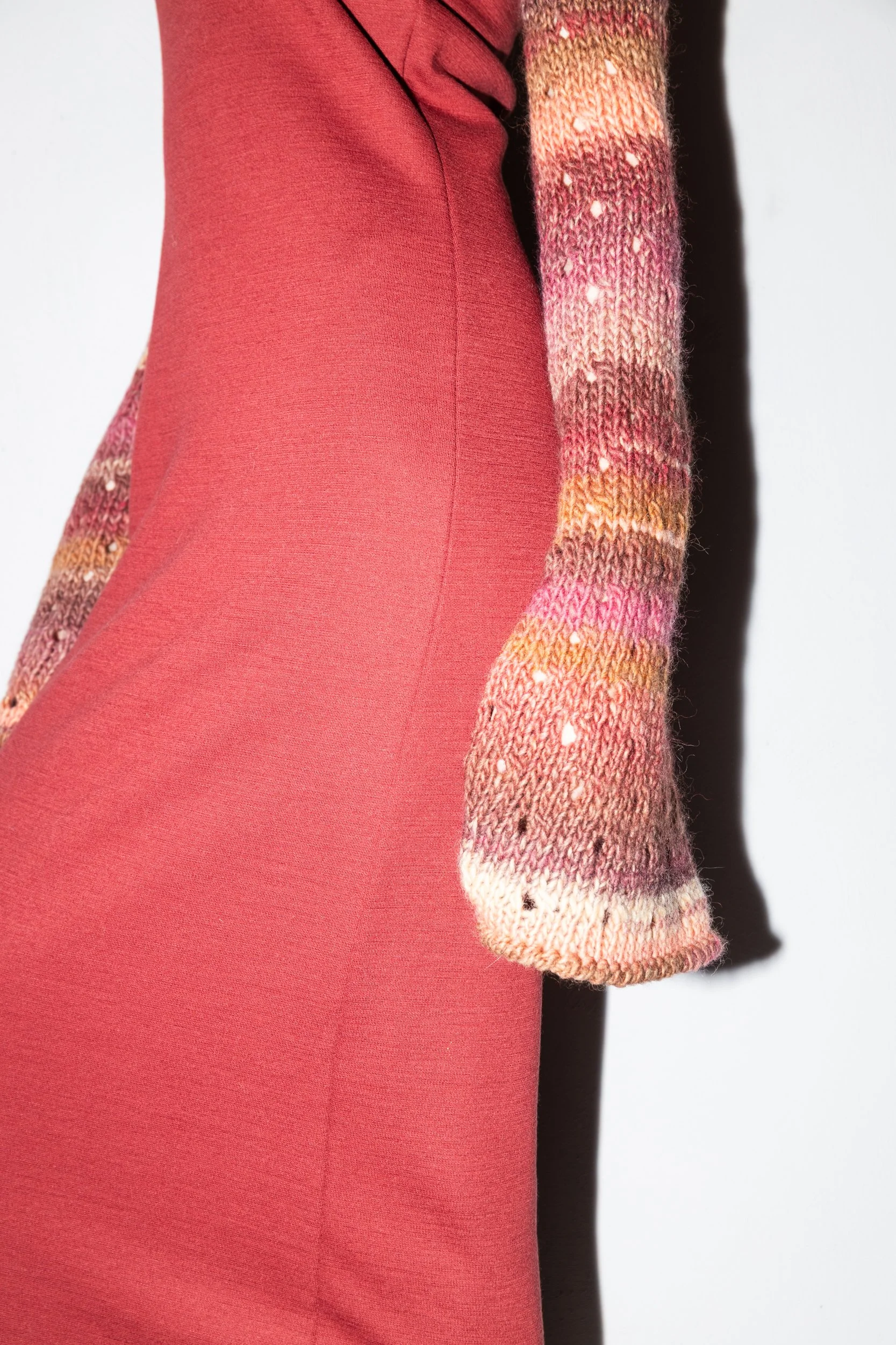 Close-up of a person wearing a red dress and a multicolored knitted sleeve.