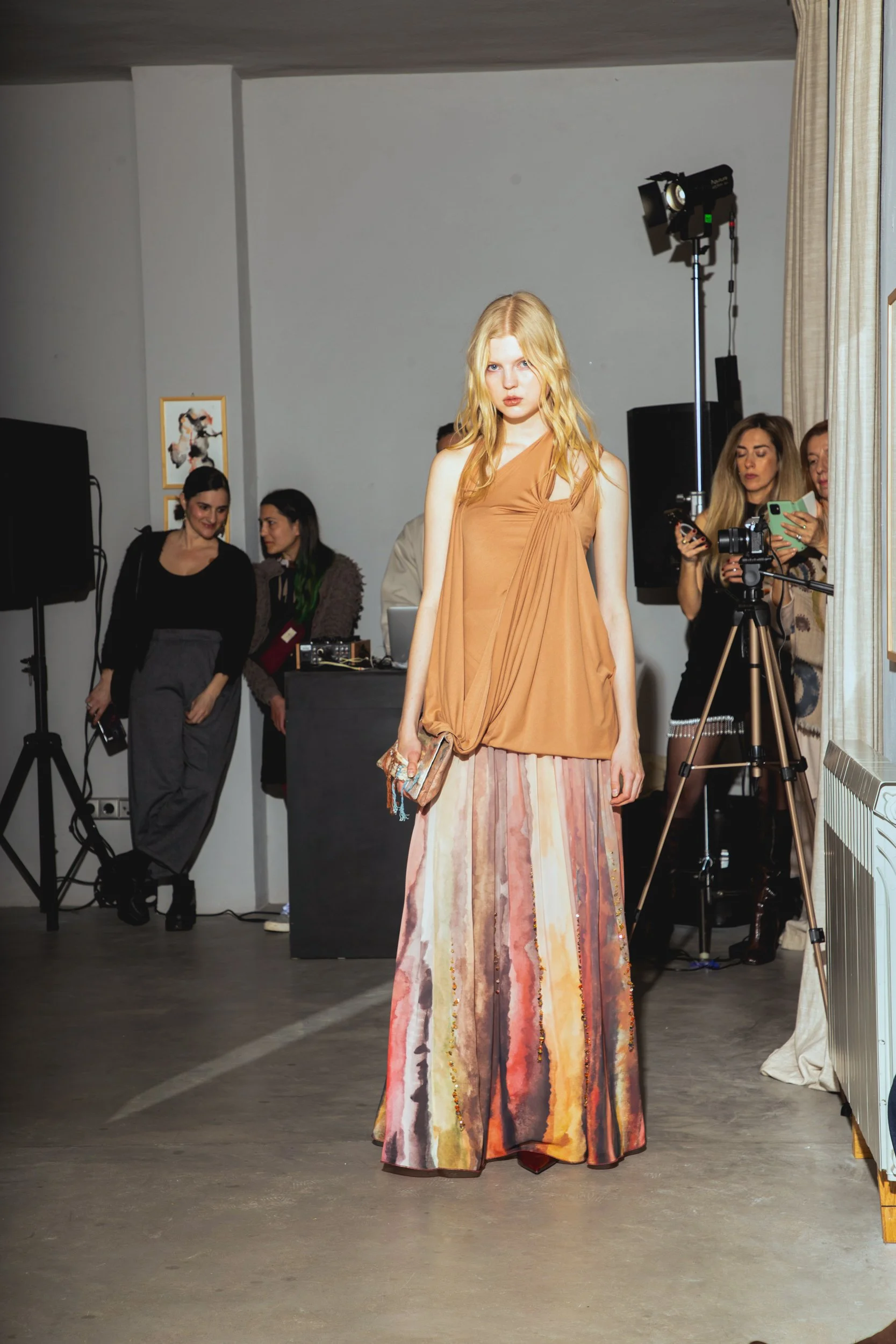 Fashion model walking runway with attendees and photographers watching in background