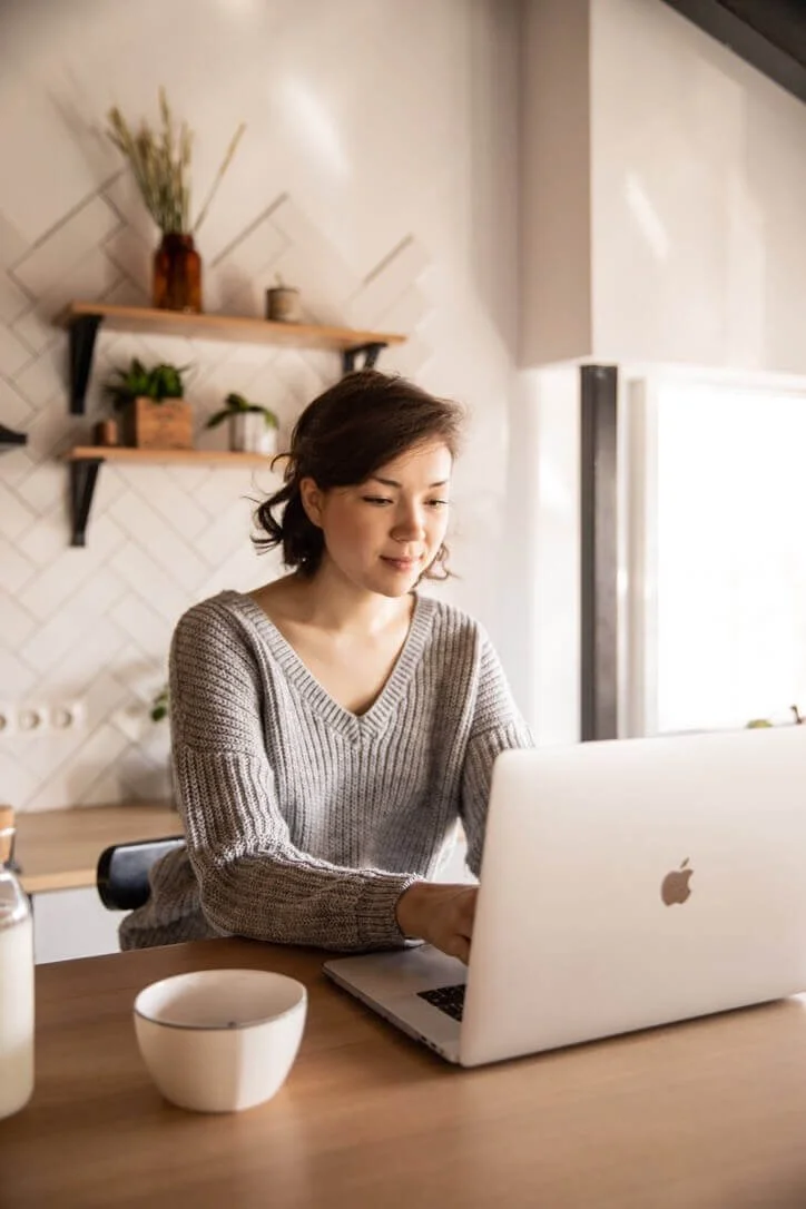 young woman wearing a sweater working on a laptop in the kitchen