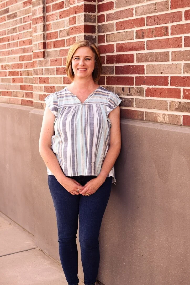 Money coach smiling confidently against brick wall in striped blouse and jeans, featured in savings challenge photo